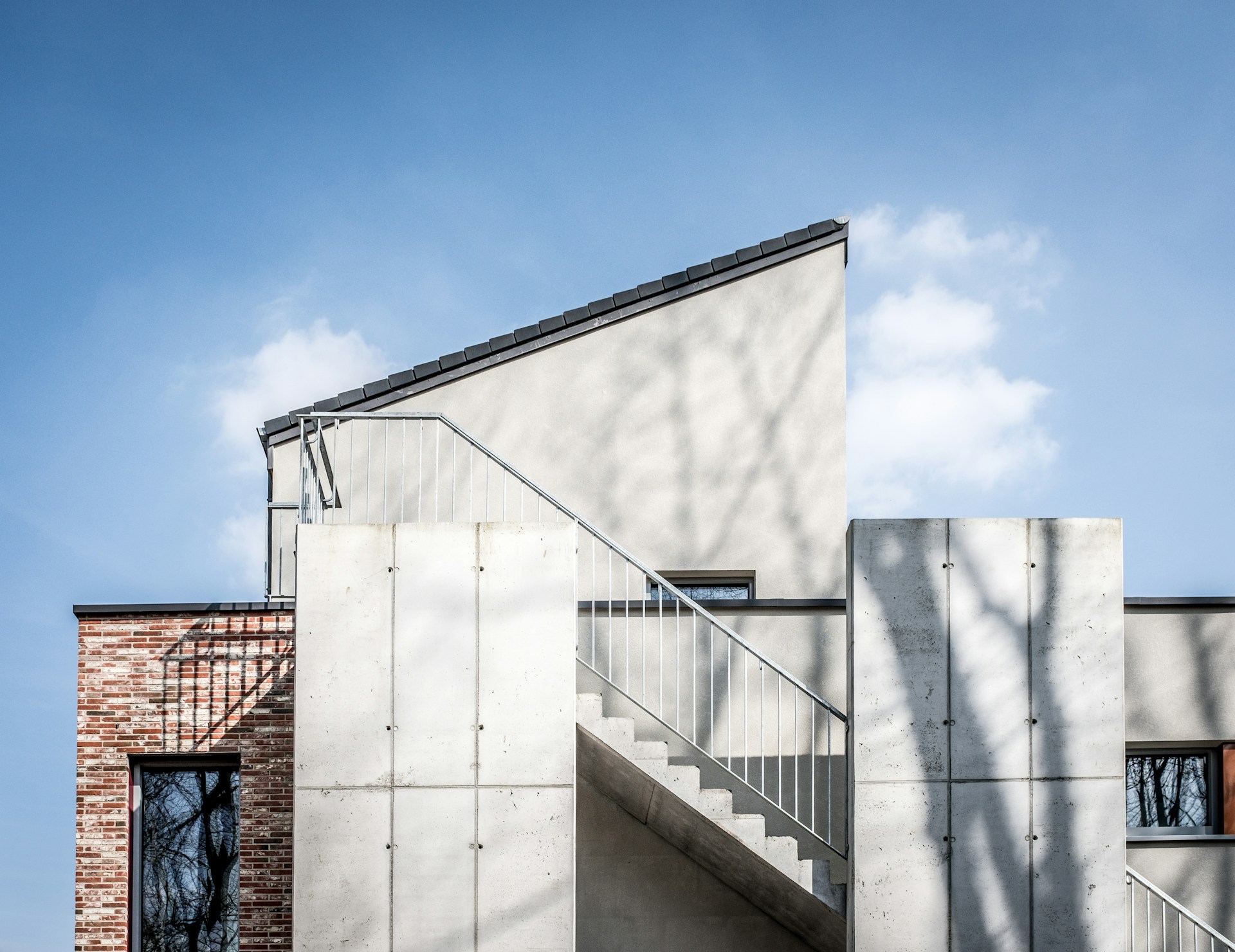 Moderne huisgevel met betonnen trap, bakstenen muur en blauw hemelachtergrond.