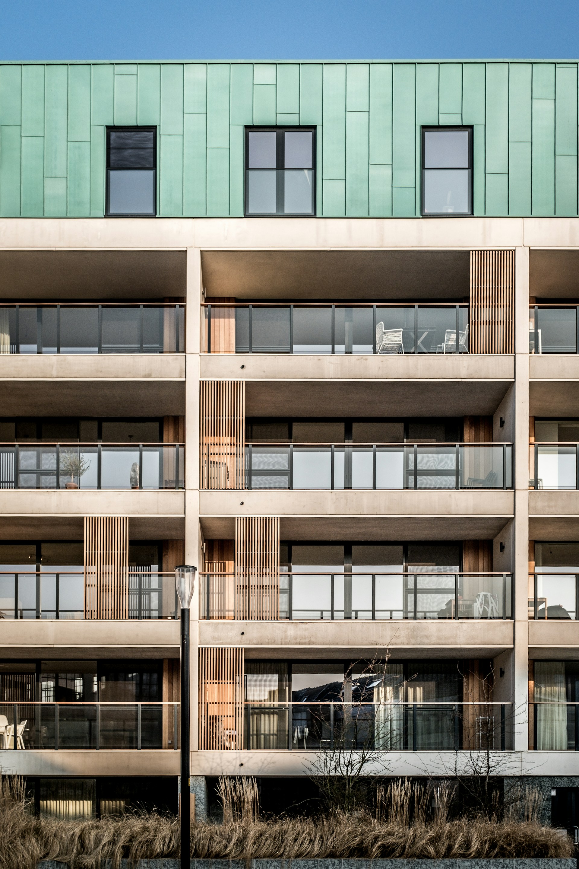 Moderne appartementen met balkons, glazen balustrades en gevelbekleding van groen metaal en hout.