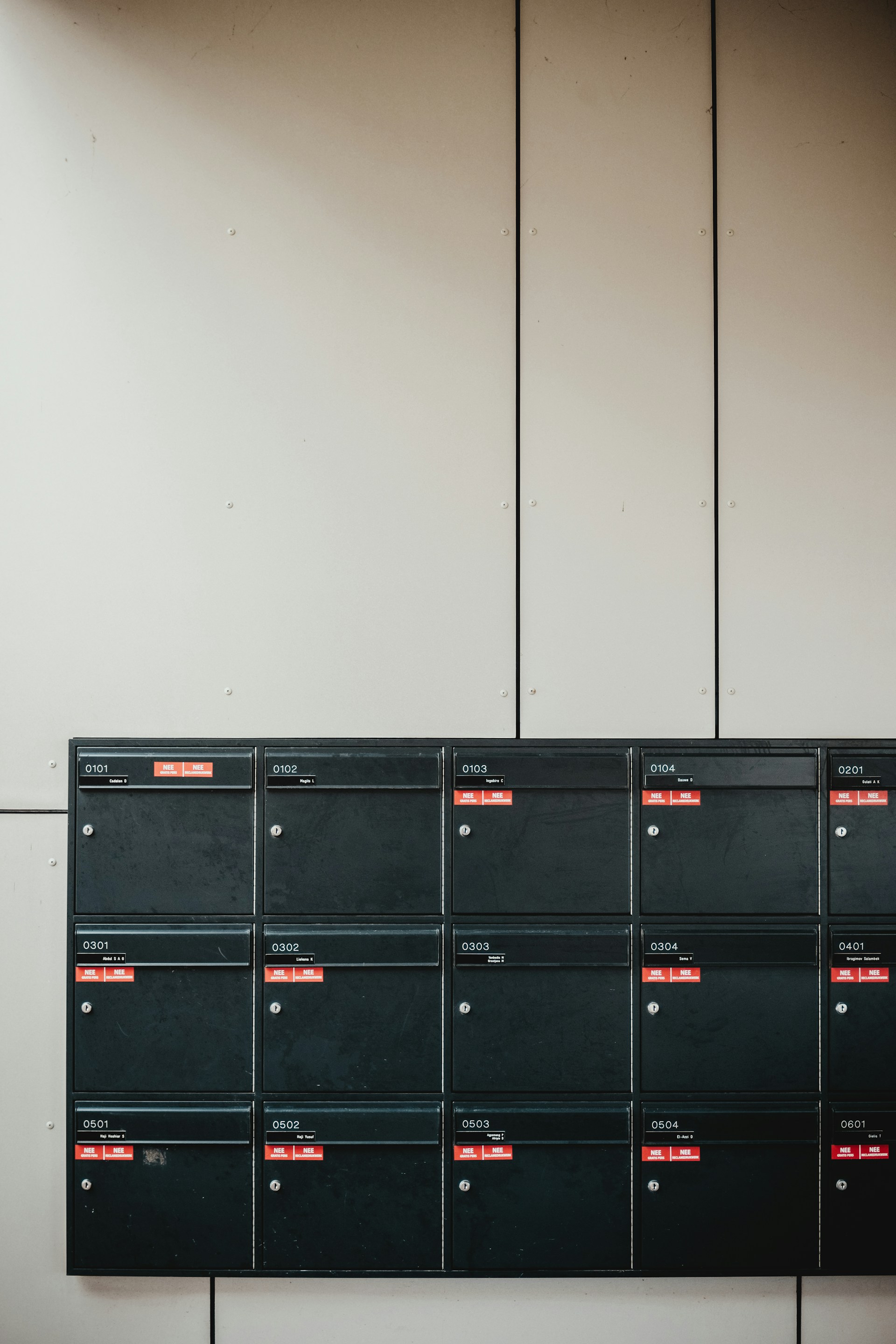 Zwarte postbussen op muur met rode stickers 'Nee Geen Reclame'.