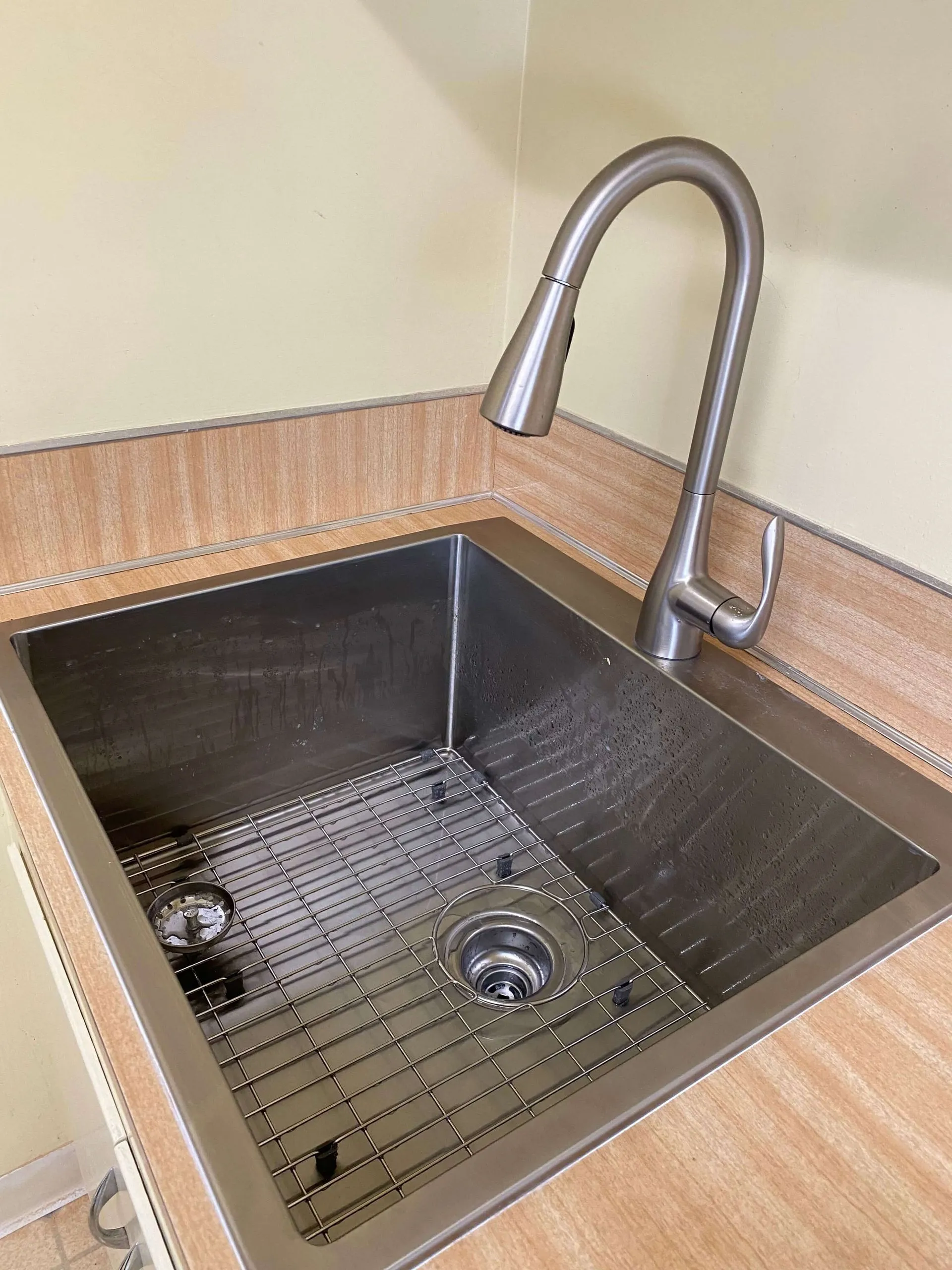 Stainless steel kitchen sink with a modern curved faucet and a metal grid at the bottom.