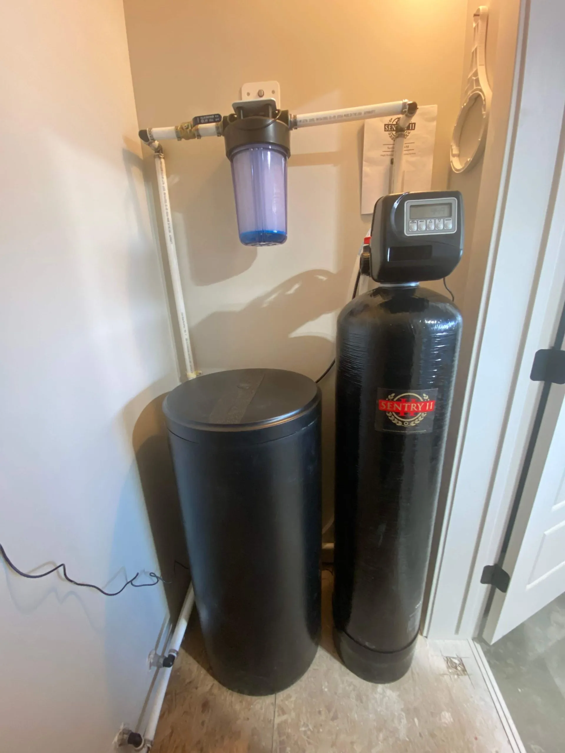 Black Sentry II water softener system with cylindrical brine tank and filter unit installed in a utility room corner.
