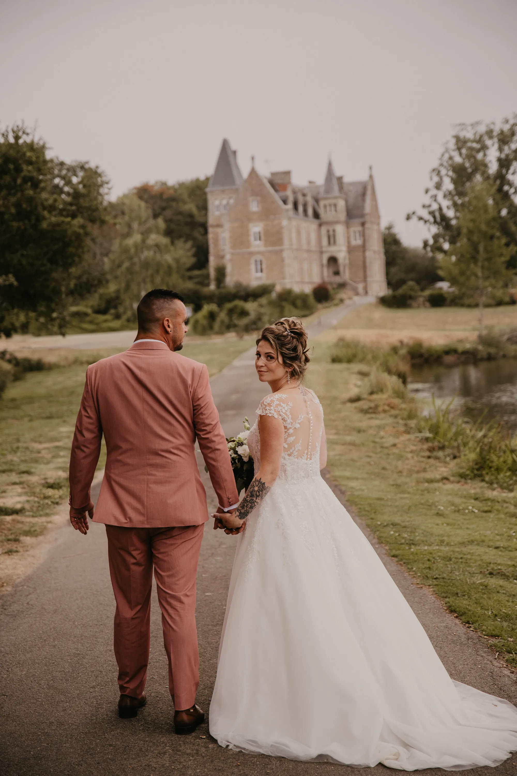 Photographe mariage Loire-Atlantique — mariés marchant dans une allée avec un château en fond