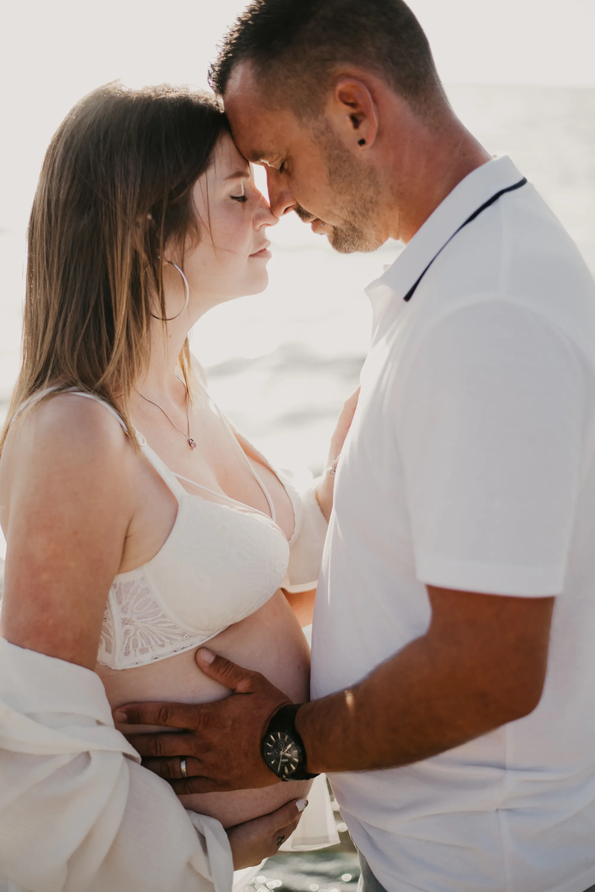Photographe maternité Loire-Atlantique -  couple de futurs parents, front contre front, avec les mains du futur papa posées sur le ventre rond de la femme enceinte