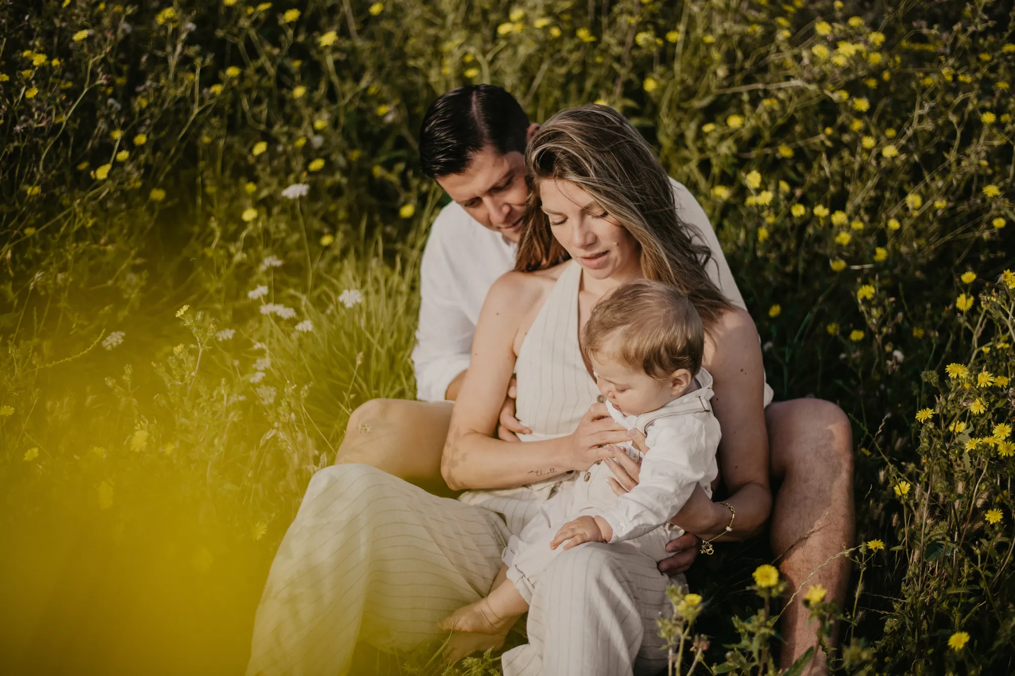Photographe maternité Loire-Atlantique — parents et petit garçon assis dans un champs de fleurs jaunes