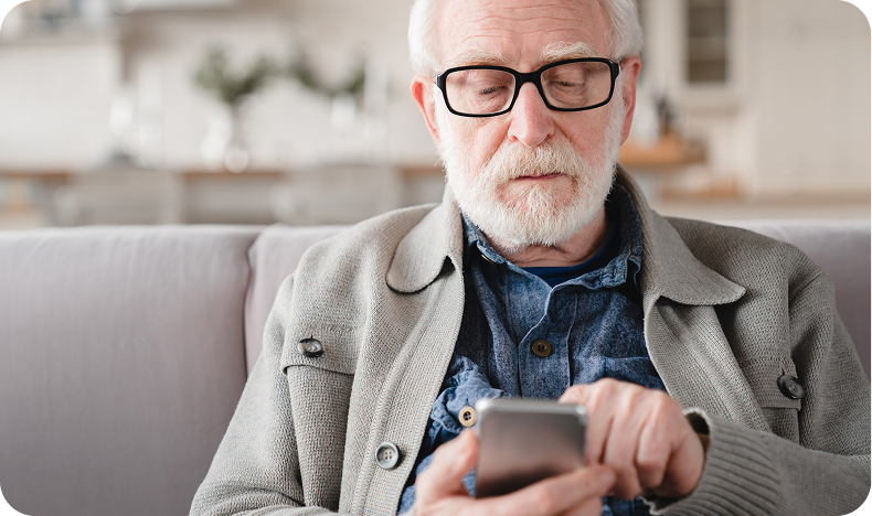 Older man with glasses using a smartphone while seated on a couch in a cozy room.