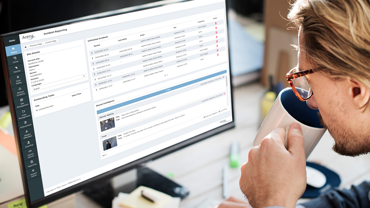 Man in glasses drinking from a mug while looking at an incident reporting software on a computer screen.