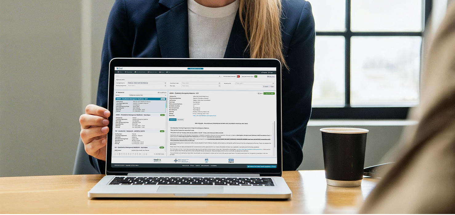 Person in blazer holding laptop showing a job vacancy webpage for pediatric emergency medicine.