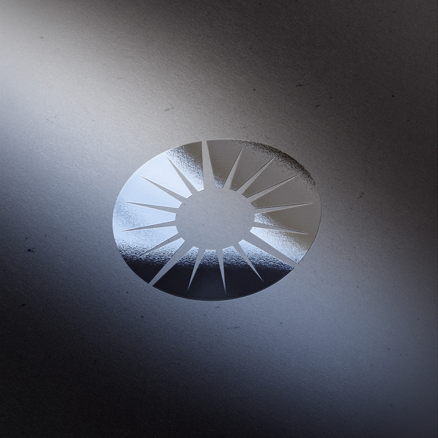 Silver circular emblem with radial cutouts on a textured gray surface under soft lighting.