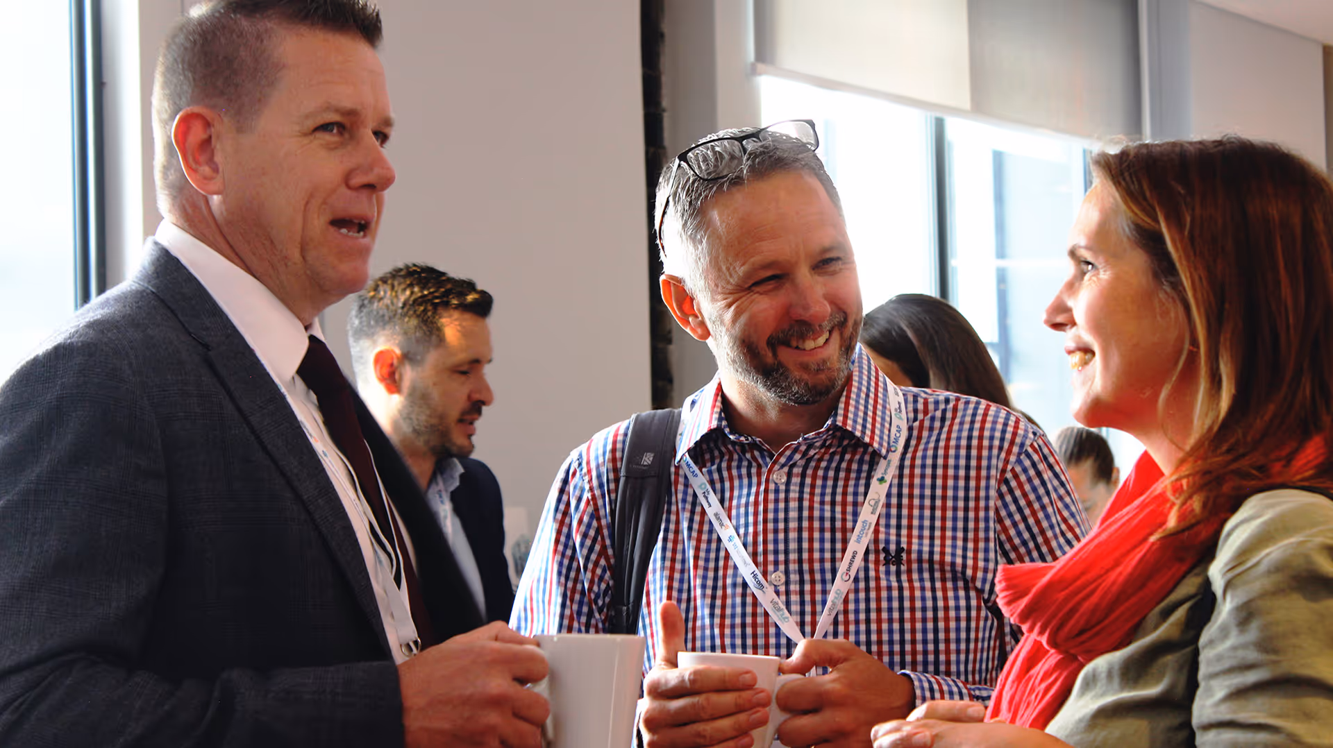 Three colleagues chatting and smiling, holding coffee cups in a well-lit office setting.