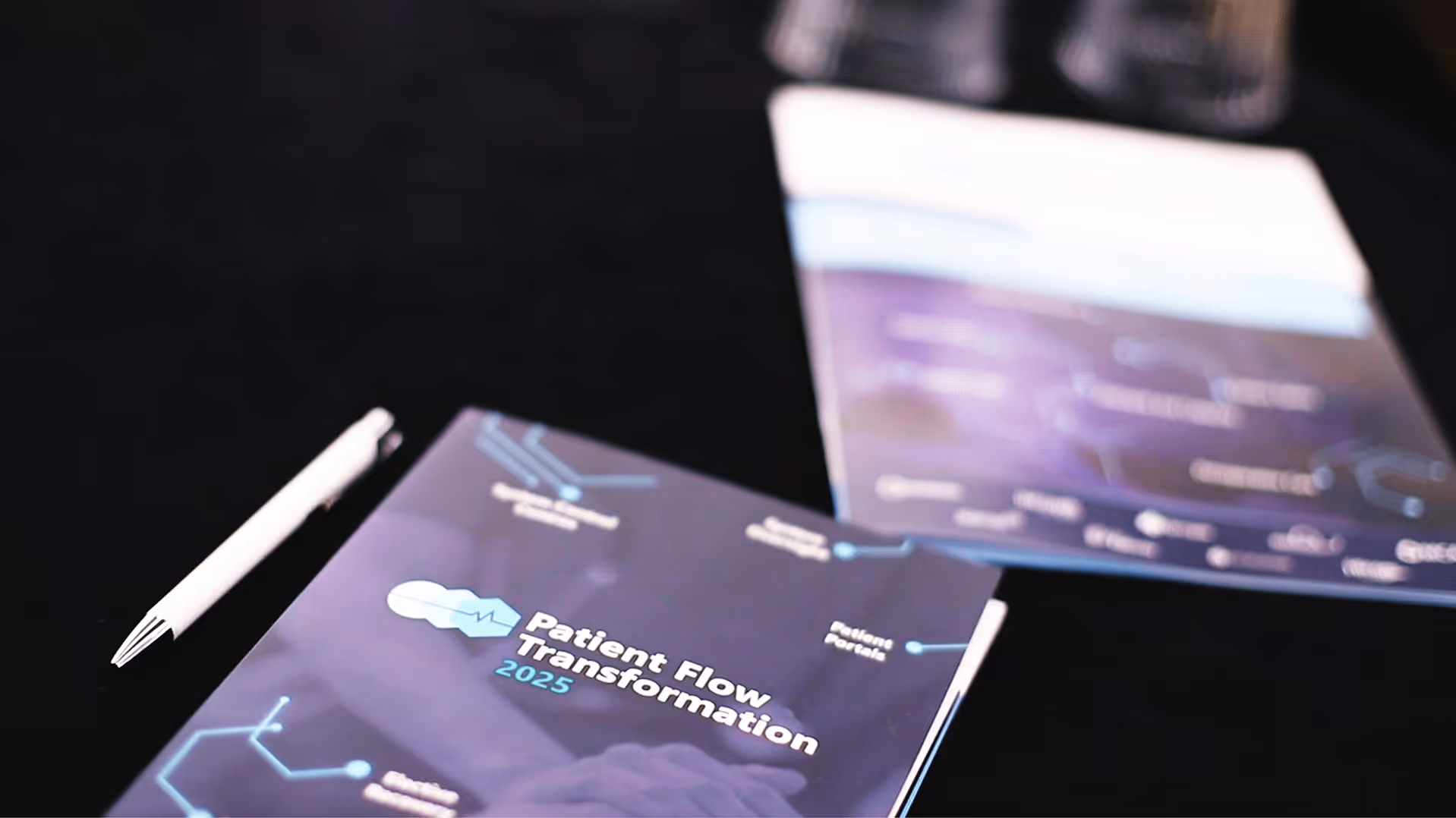 Brochure titled 'Patient Flow Transformation 2025' with a white pen on a black surface.