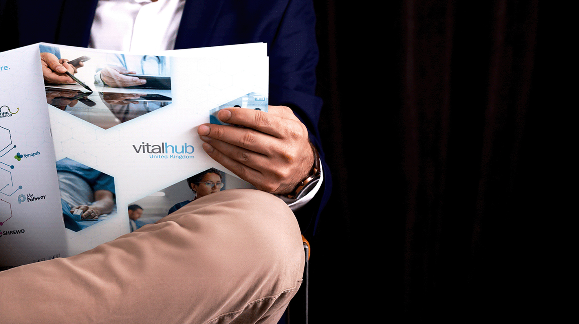 Person in navy blazer and khaki pants reading a VitalHub United Kingdom brochure.