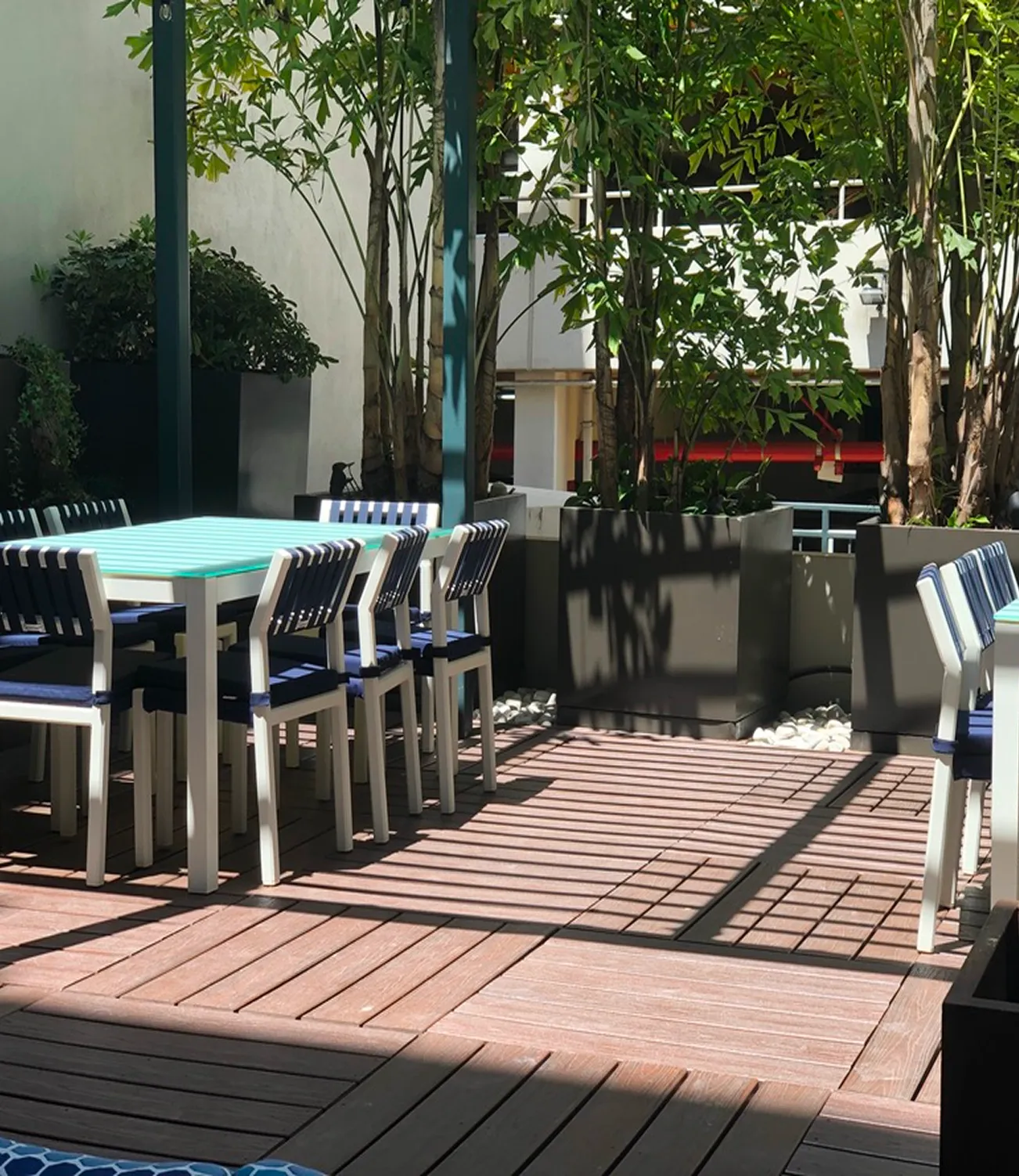wood deck, teal dining table, navy and white chairs, lush landscaping