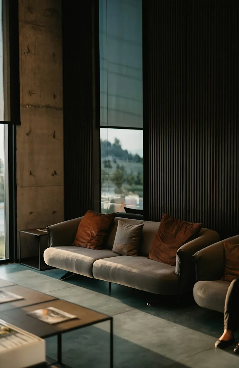 dramatic double-height space, concrete columns, velvet sofa with rust cushions, hanging chair