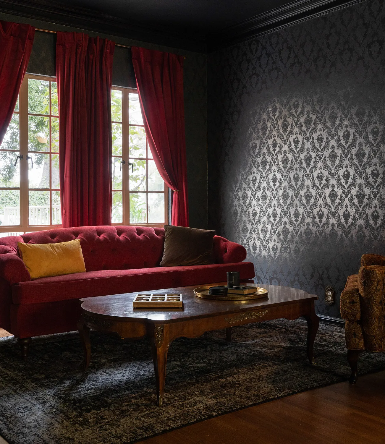 crimson tufted Chesterfield sofa, damask wallpaper, red velvet drapes, wood coffee table (Magic Castle-era style)