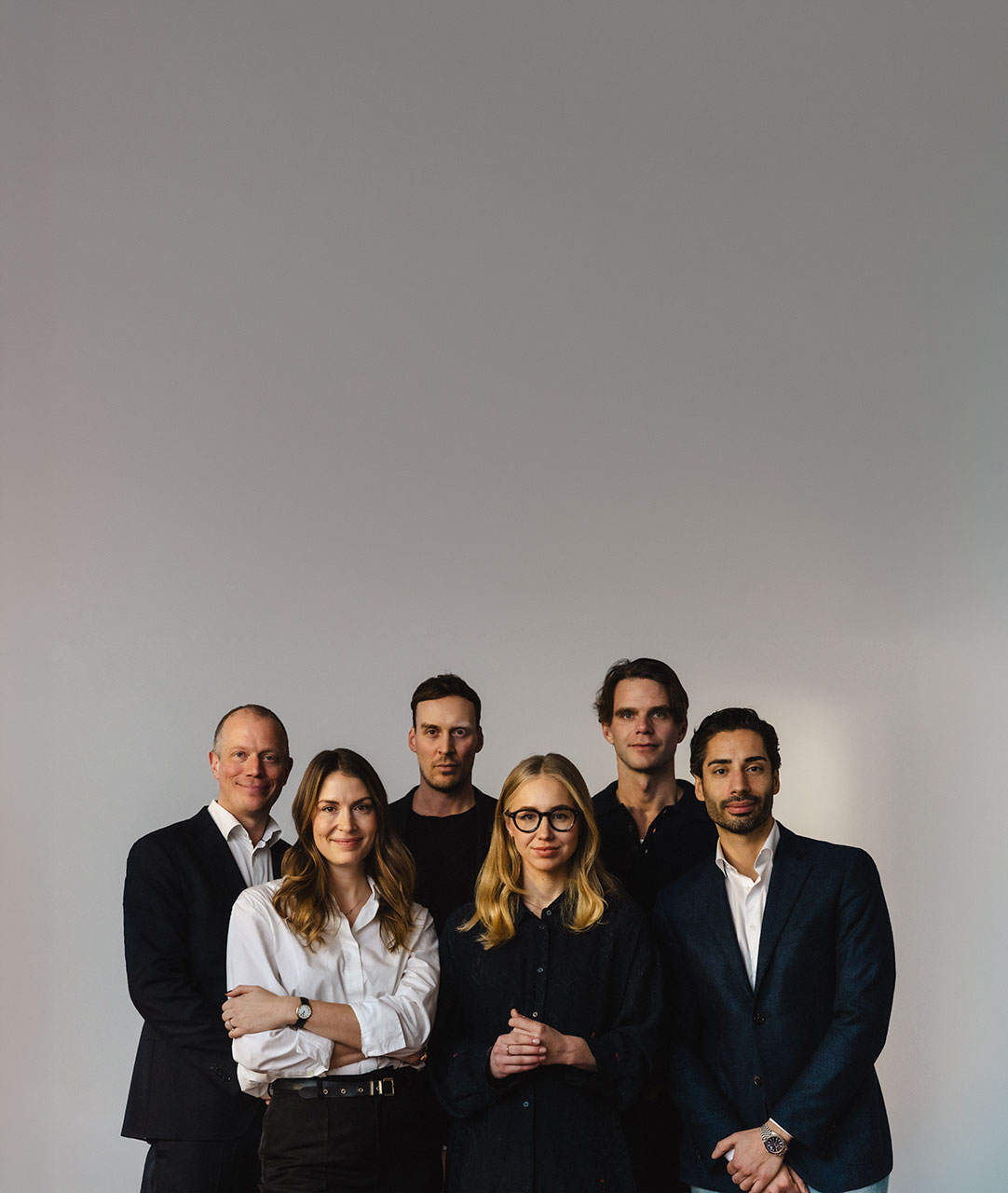 Group portrait of three men and two women standing together against a plain light gray background.
