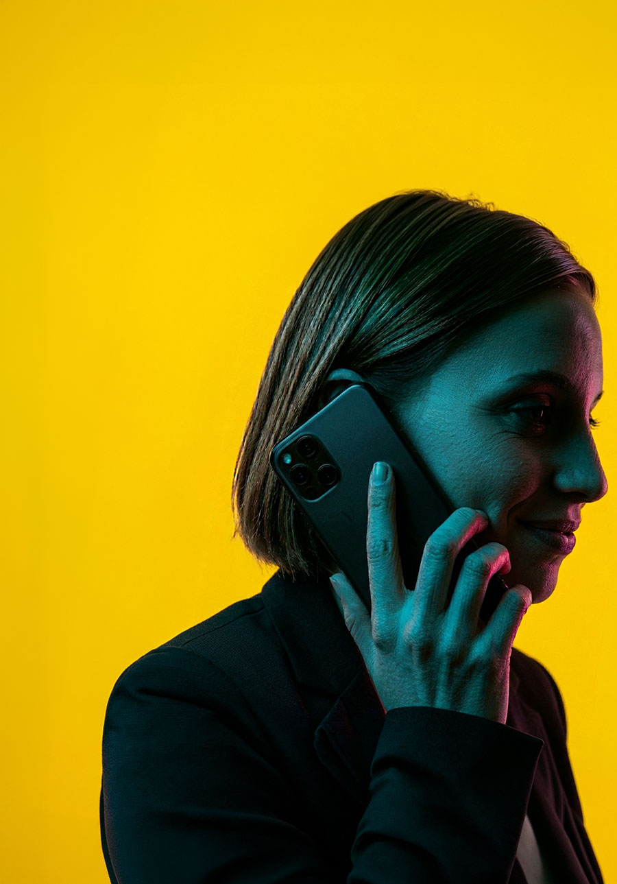 Woman with short hair holding a smartphone to her ear against a bright yellow background.