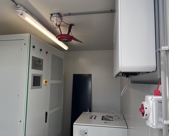 Technische ruimte met Grid Stabilizer apparaat, controles en een rode blusser aan het plafond.