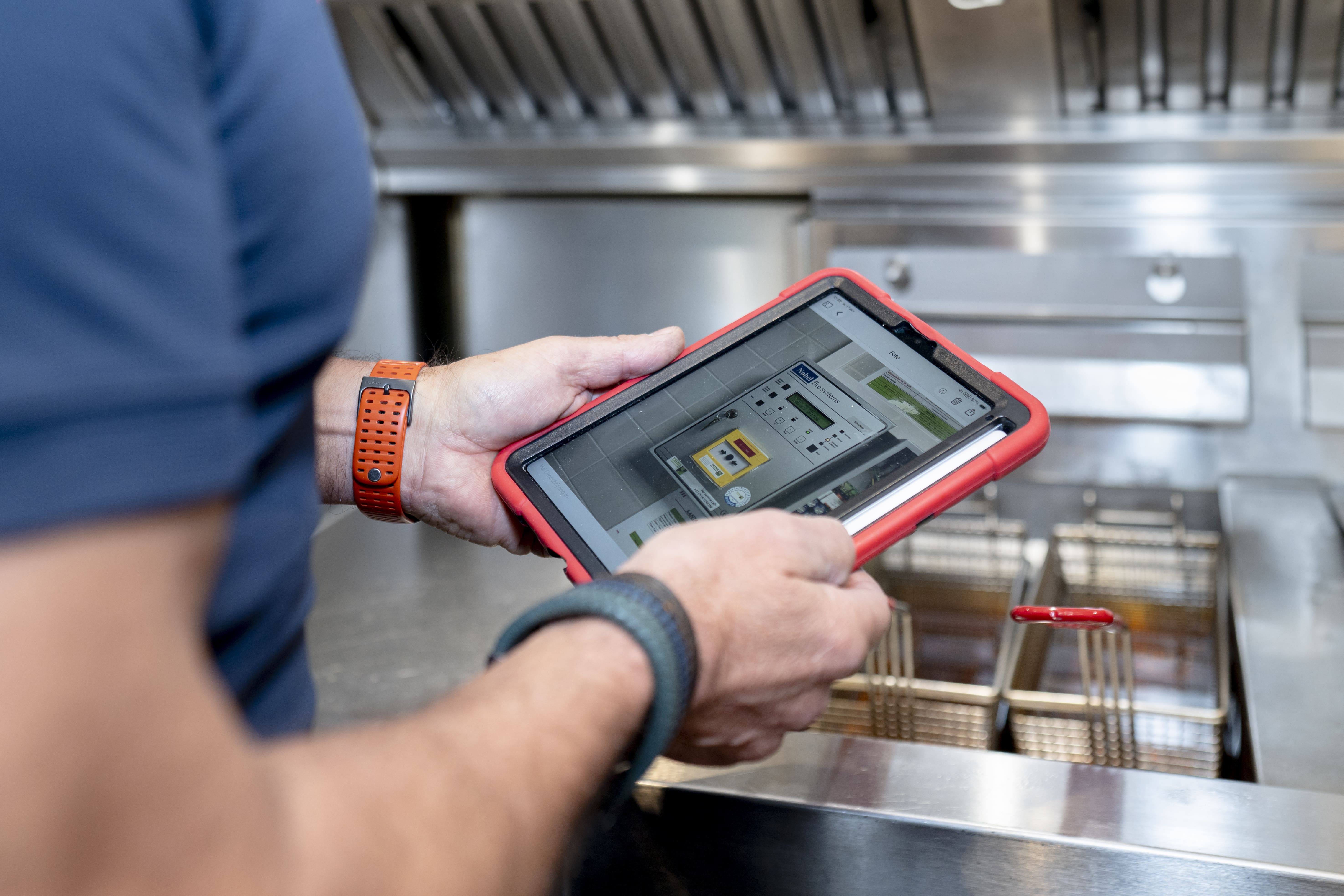 Persoon die een tablet met een bedieningspaneel vastheeft boven een professionele frituurpan.