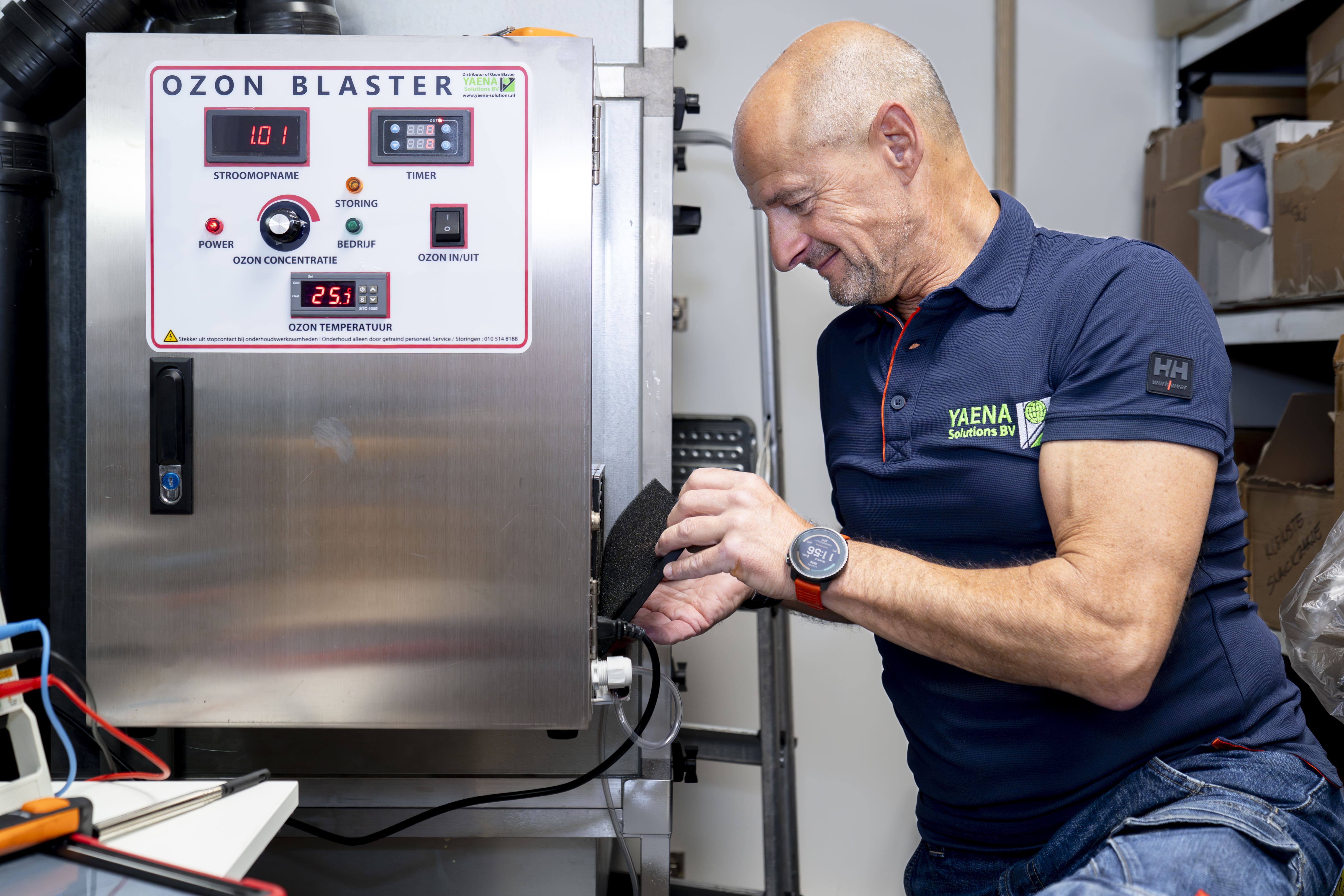 Man in blauw poloshirt met Yaena Solutions BV-logo werkt aan een RVS ozonmachine met digitale displays.