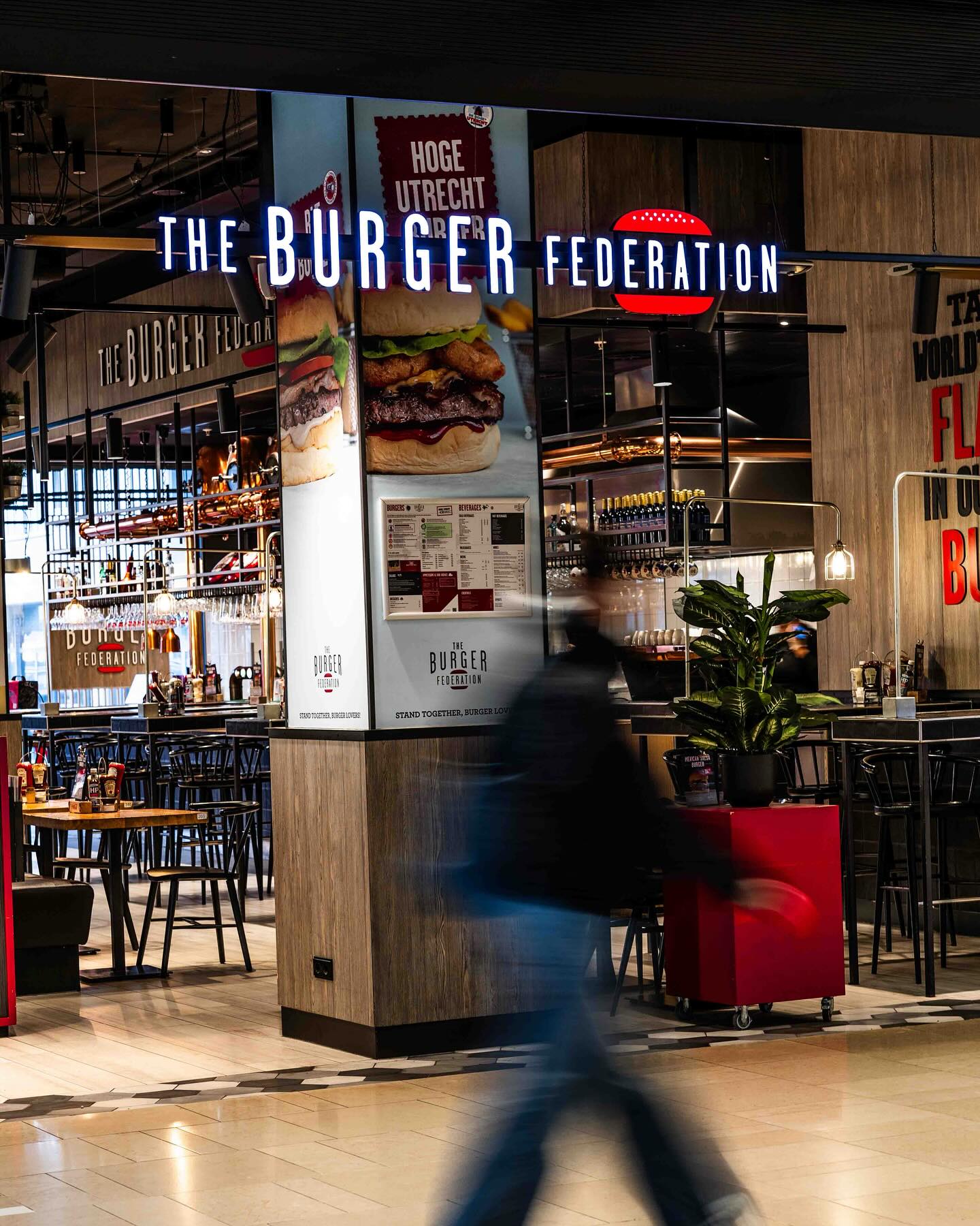 Binnenin een restaurant van The Burger Federation met een bewegende persoon op de voorgrond.