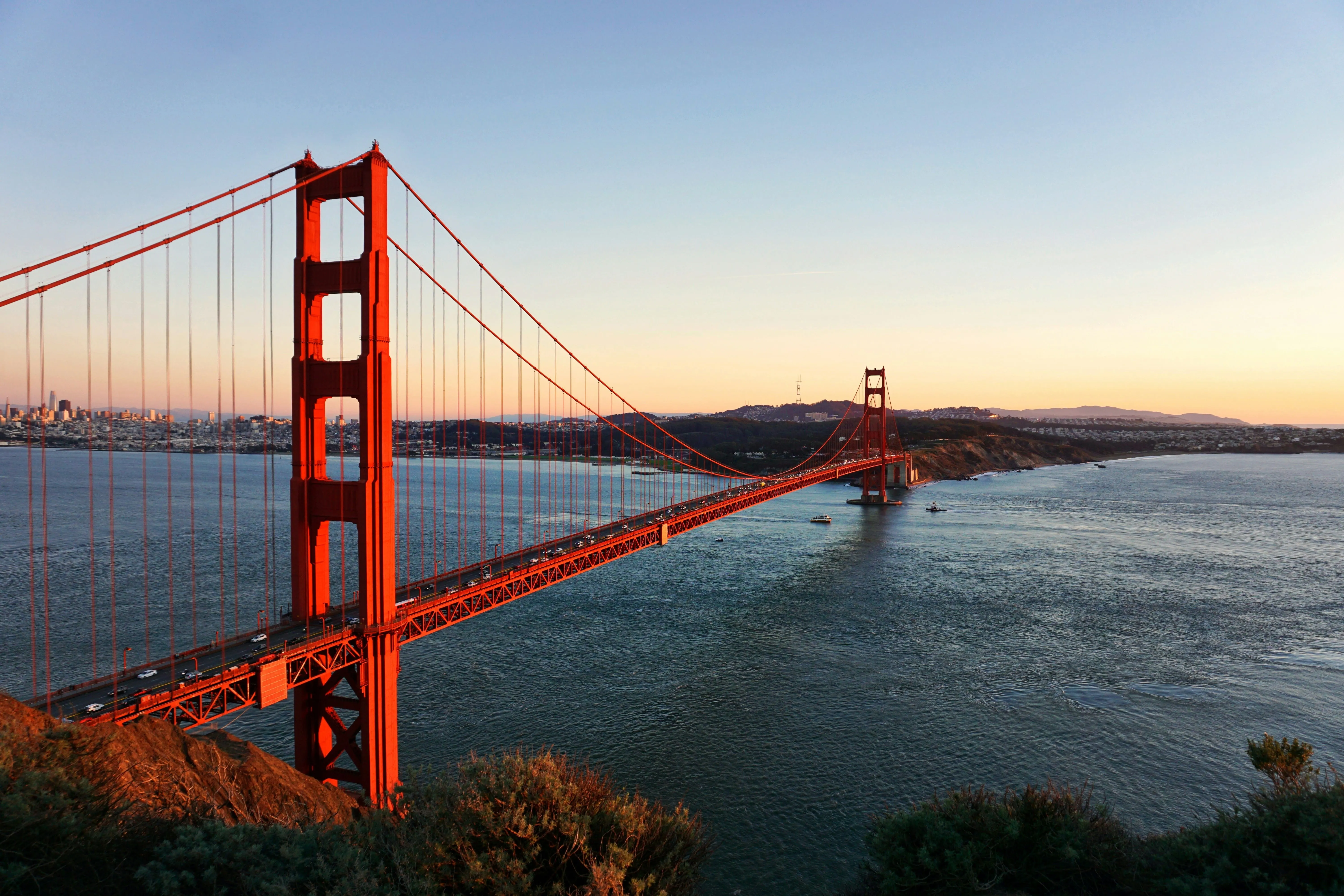 Le Golden Gate Bridge à San Francisco au coucher du soleil, au‑dessus de l’eau calme et de la skyline de la ville.
