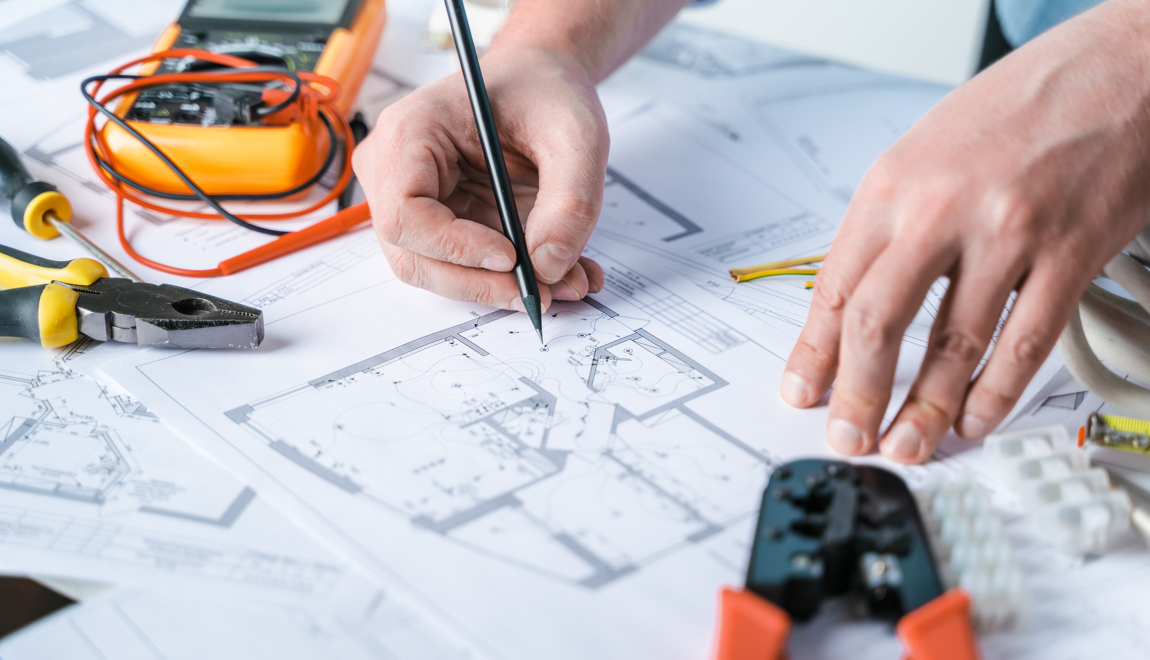 Mains annotant des plans techniques électriques avec outils de mesure sur table de bureau d'études
