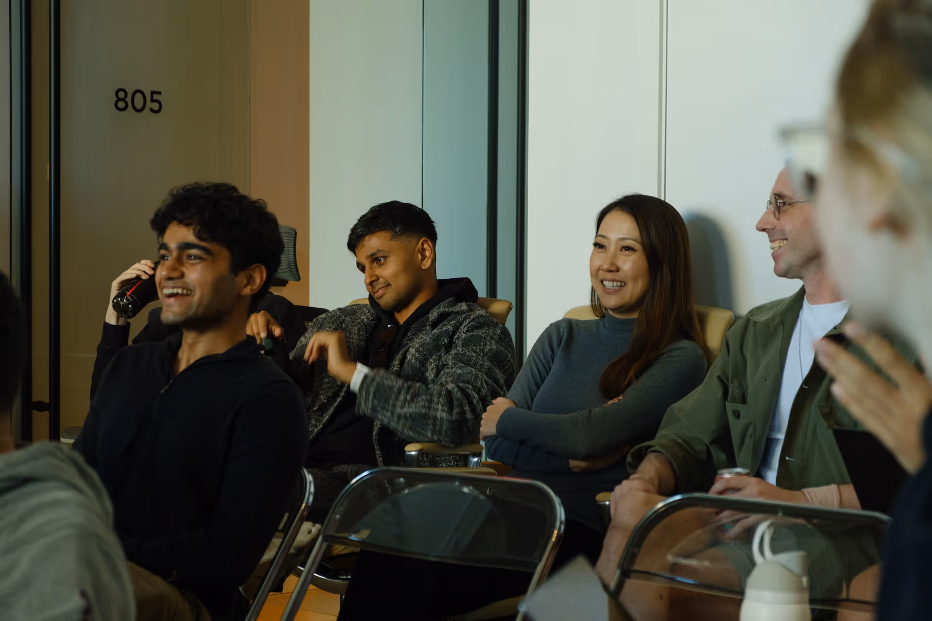 Group of diverse young adults sitting and smiling in a casual indoor setting.