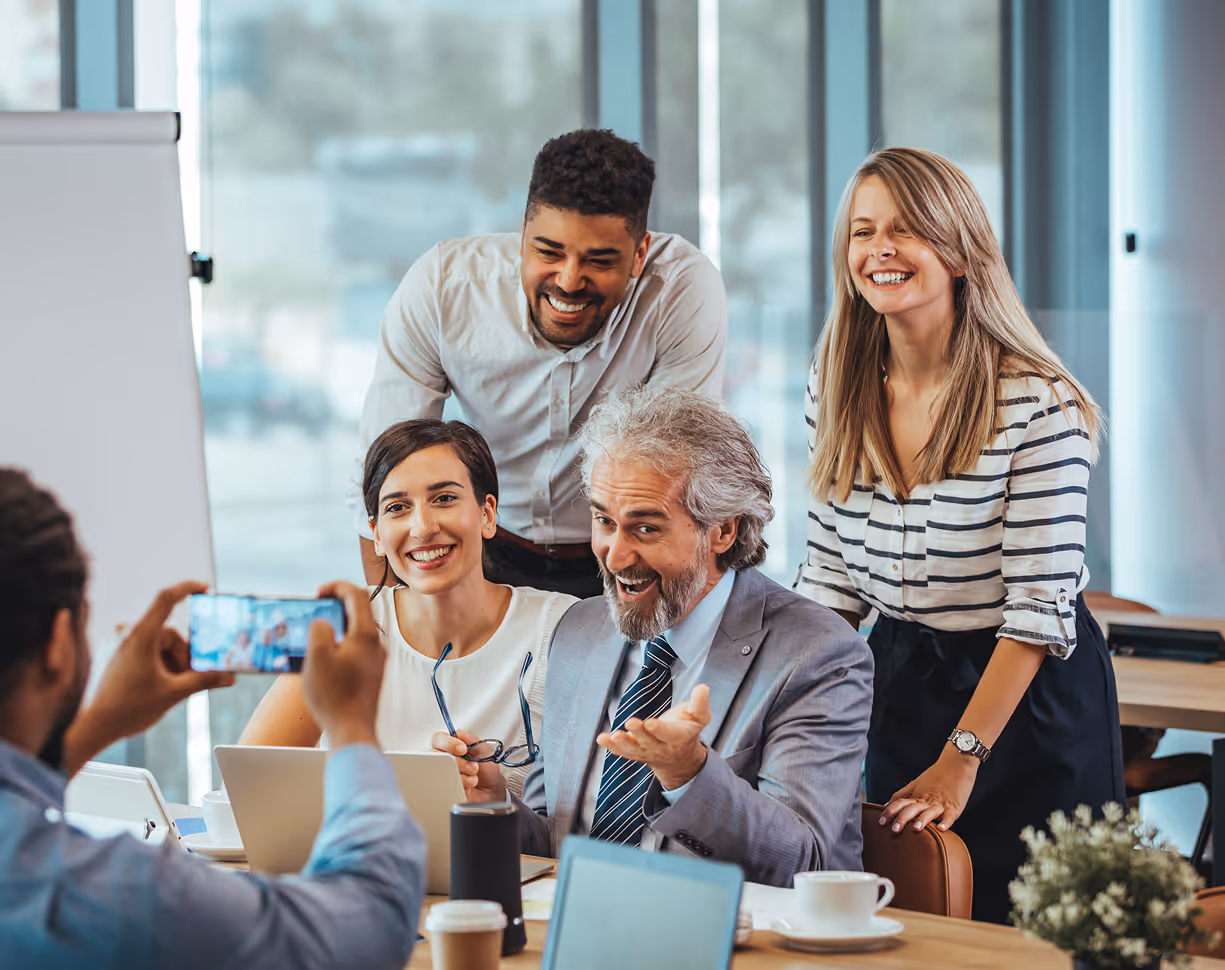 Groupe de collègues souriants posant pour une photo dans un bureau moderne avec ordinateurs portables et plantes.