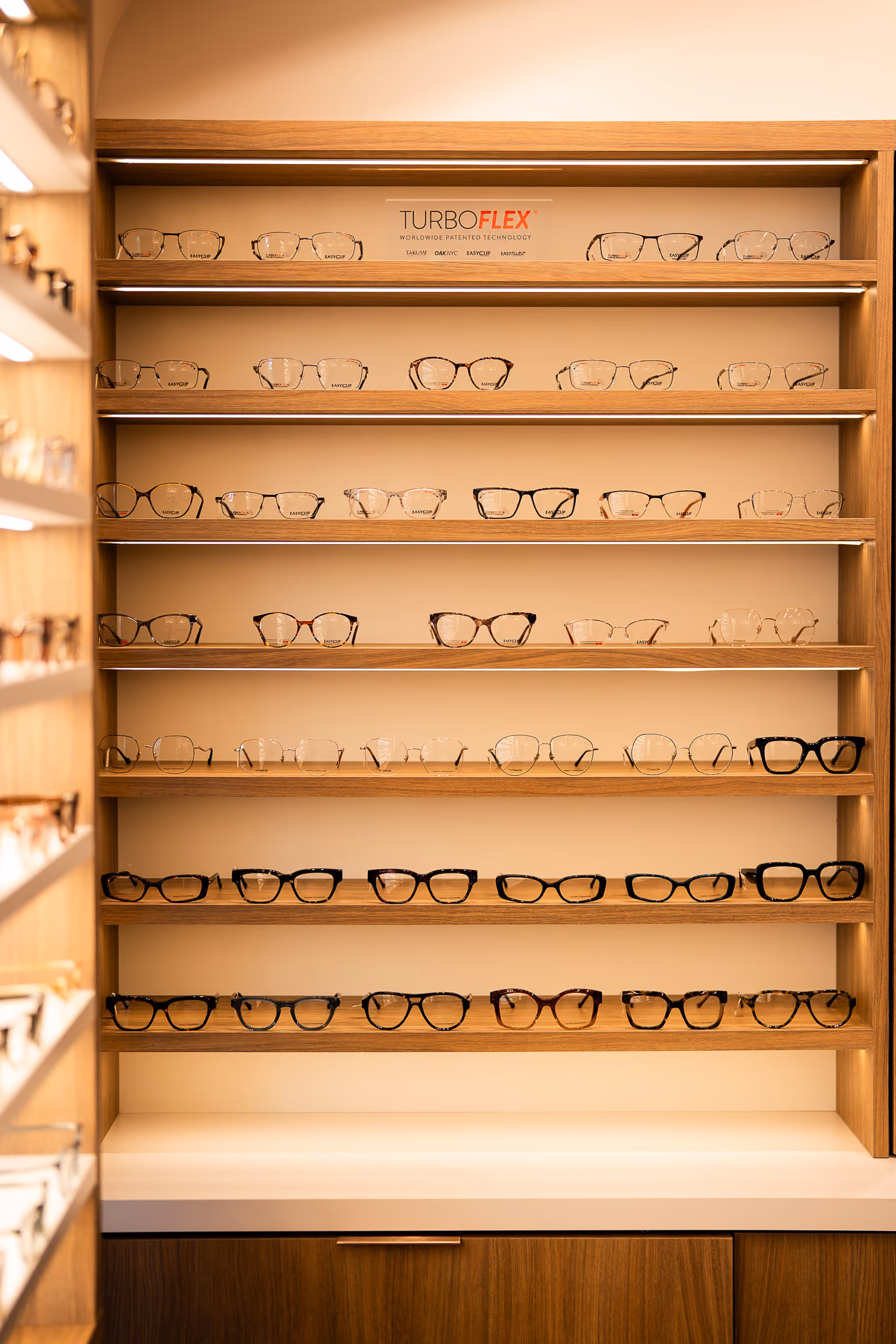 Illuminated wooden shelves lined with eyeglass frames at Vision Care Woodward.