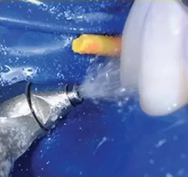 Close-up of a dental tool spraying water onto a tooth during a dental cleaning procedure.
