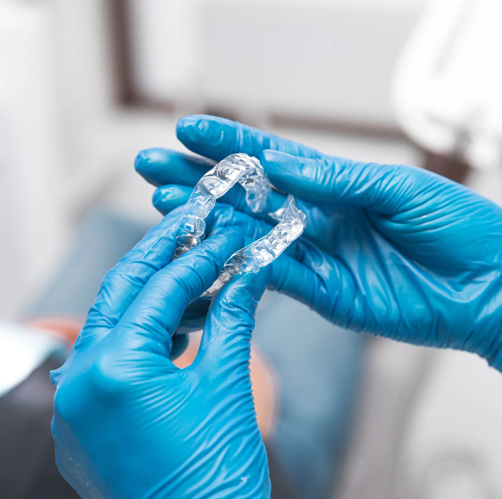 Hands in blue gloves holding clear dental aligners used for teeth straightening.