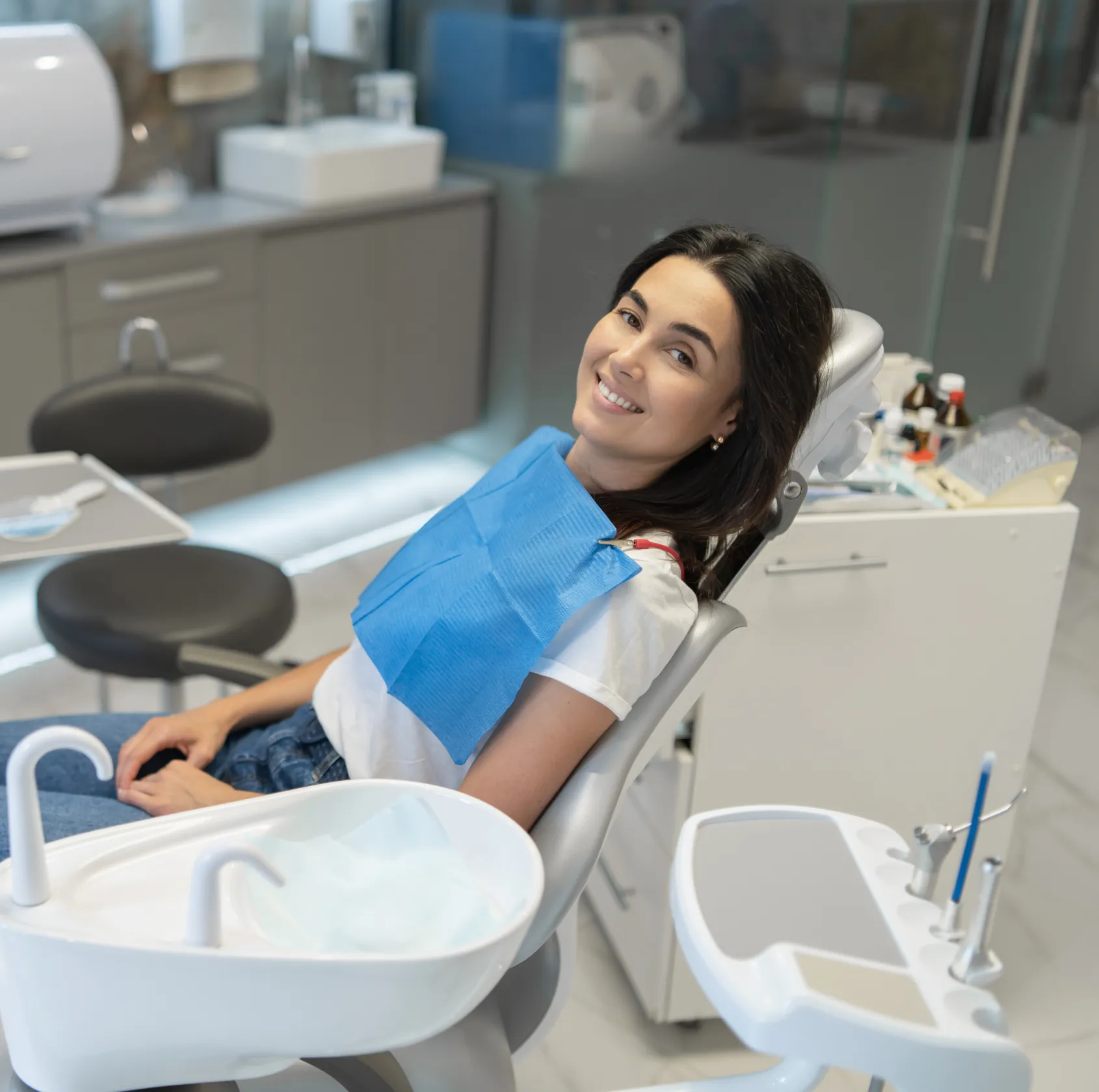 Smiling woman reclining in a dental chair with a blue protective bib in a modern dental clinic.