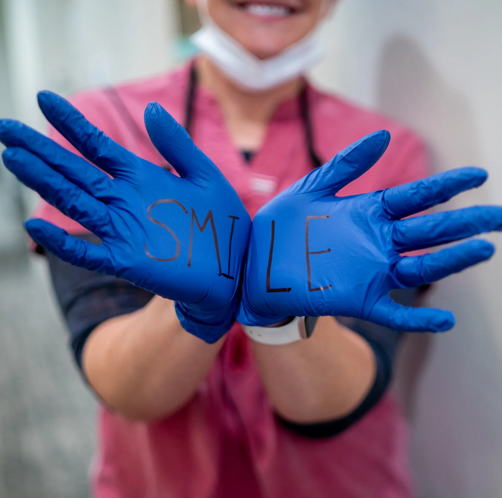 Person wearing blue gloves with the word 'SMILE' written across the palms.