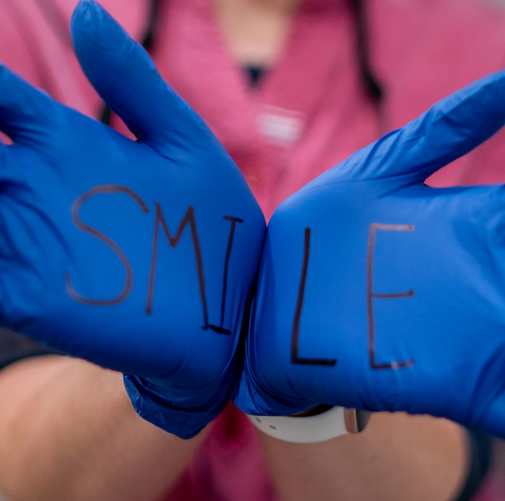 Hands wearing blue medical gloves with the word 'SMILE' written across the palms.