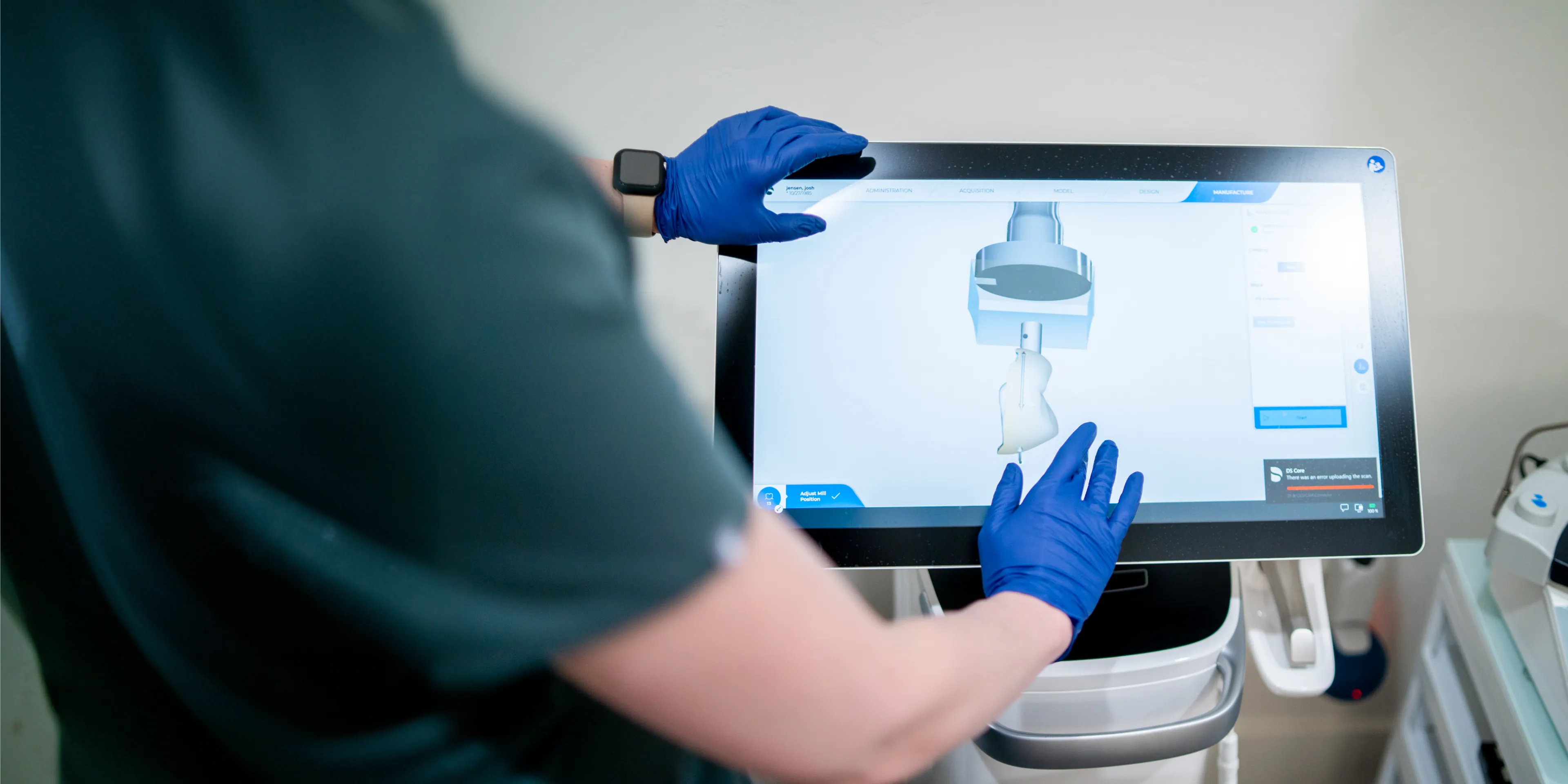 Person wearing blue gloves interacting with a touchscreen displaying a 3D model and manufacturing interface.