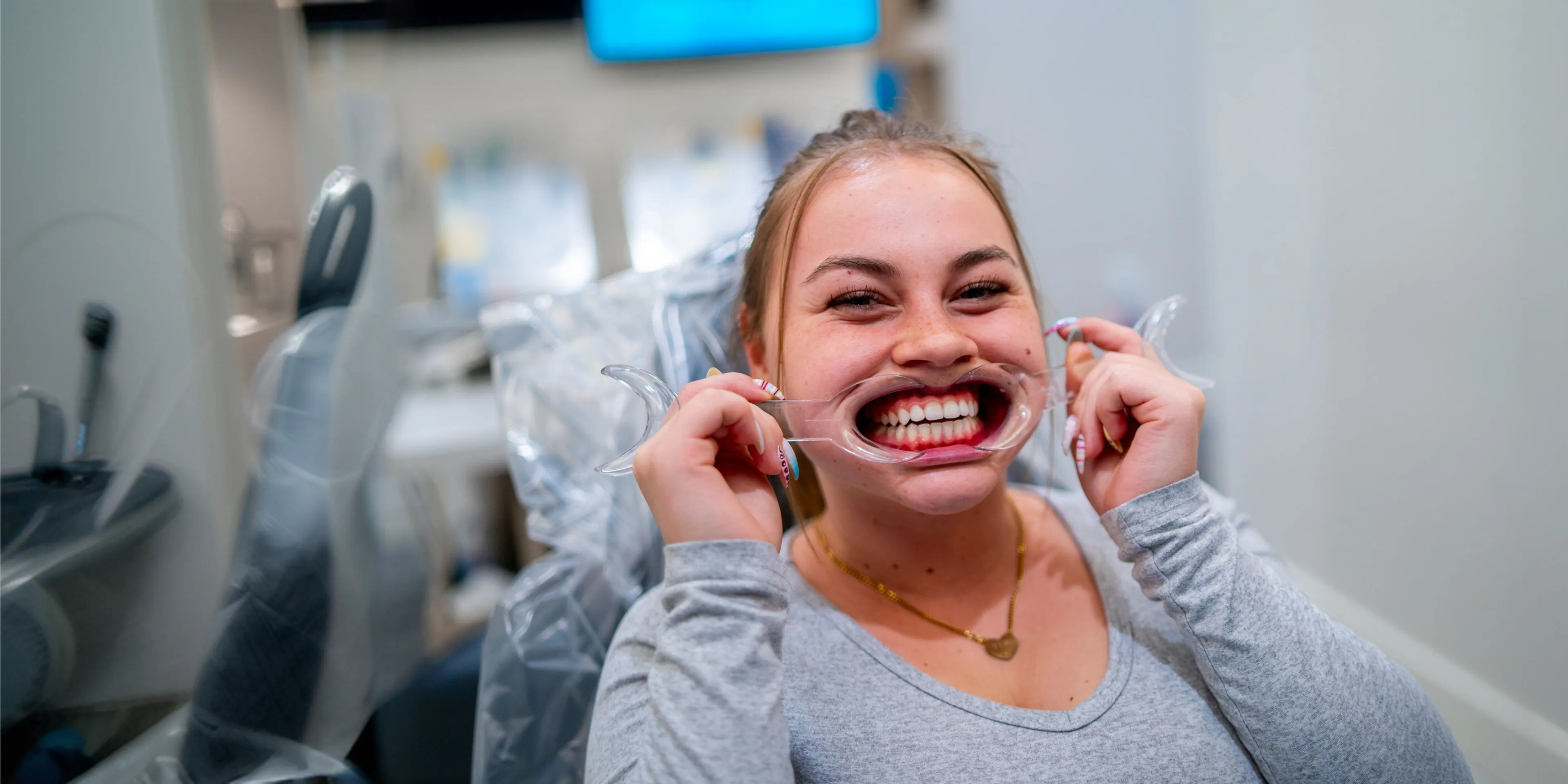 Smiling woman using a dental cheek retractor to show her teeth in a dental clinic.