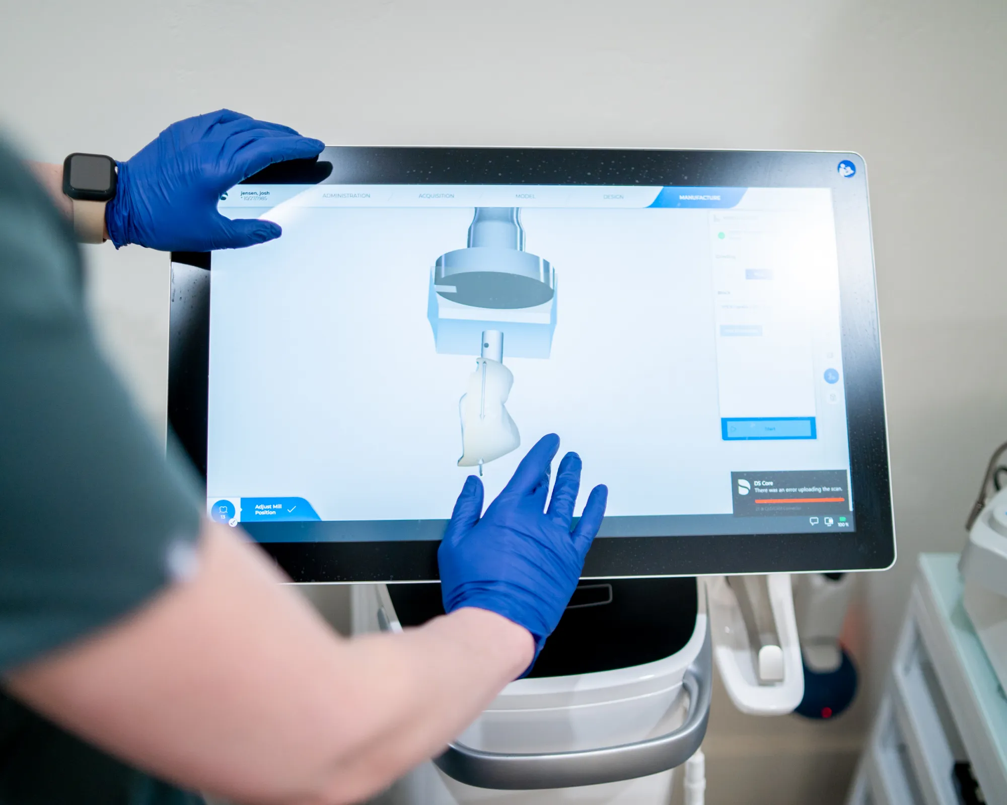 Person wearing blue gloves interacting with a touchscreen displaying 3D dental milling software.