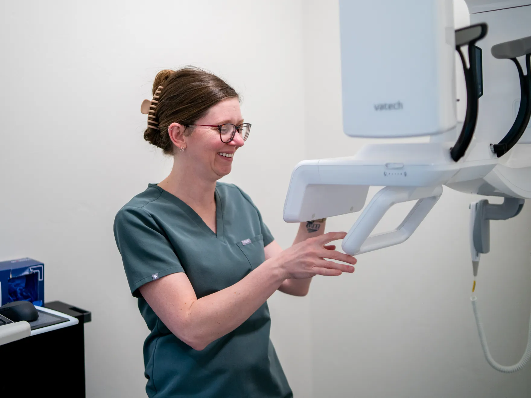 Healthcare professional in green scrubs adjusting a Vatech medical imaging device.