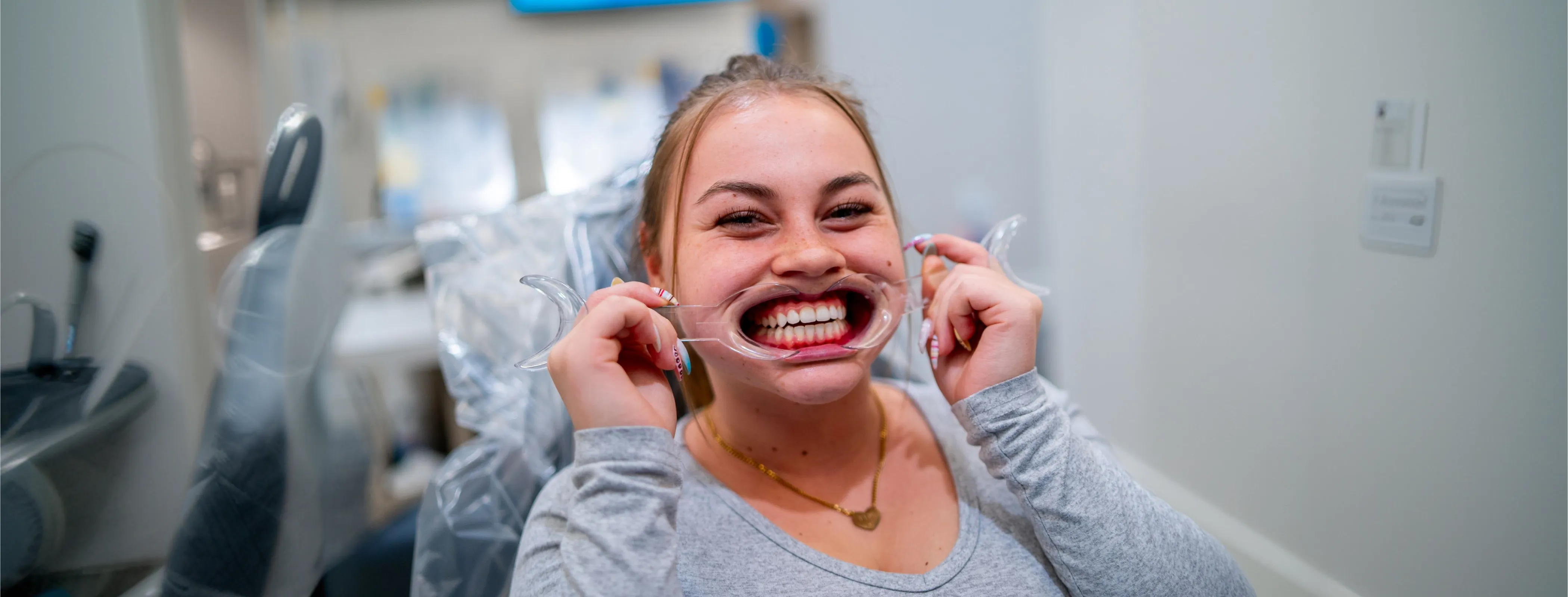 Young woman at dental office holding a cheek retractor to show her teeth while smiling.