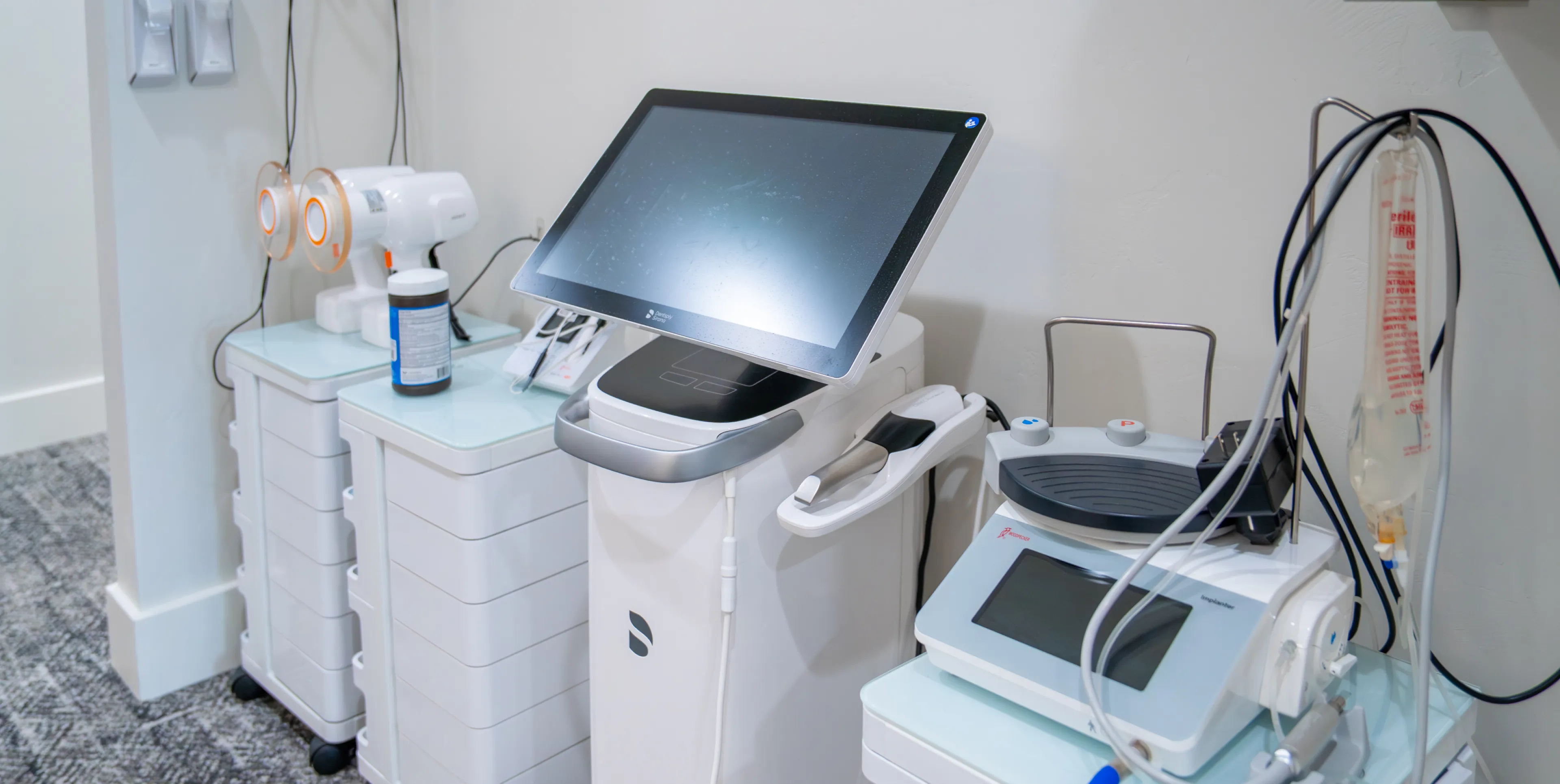 Modern medical or cosmetic equipment on white carts with digital screens and connected handheld devices in a clinical setting.