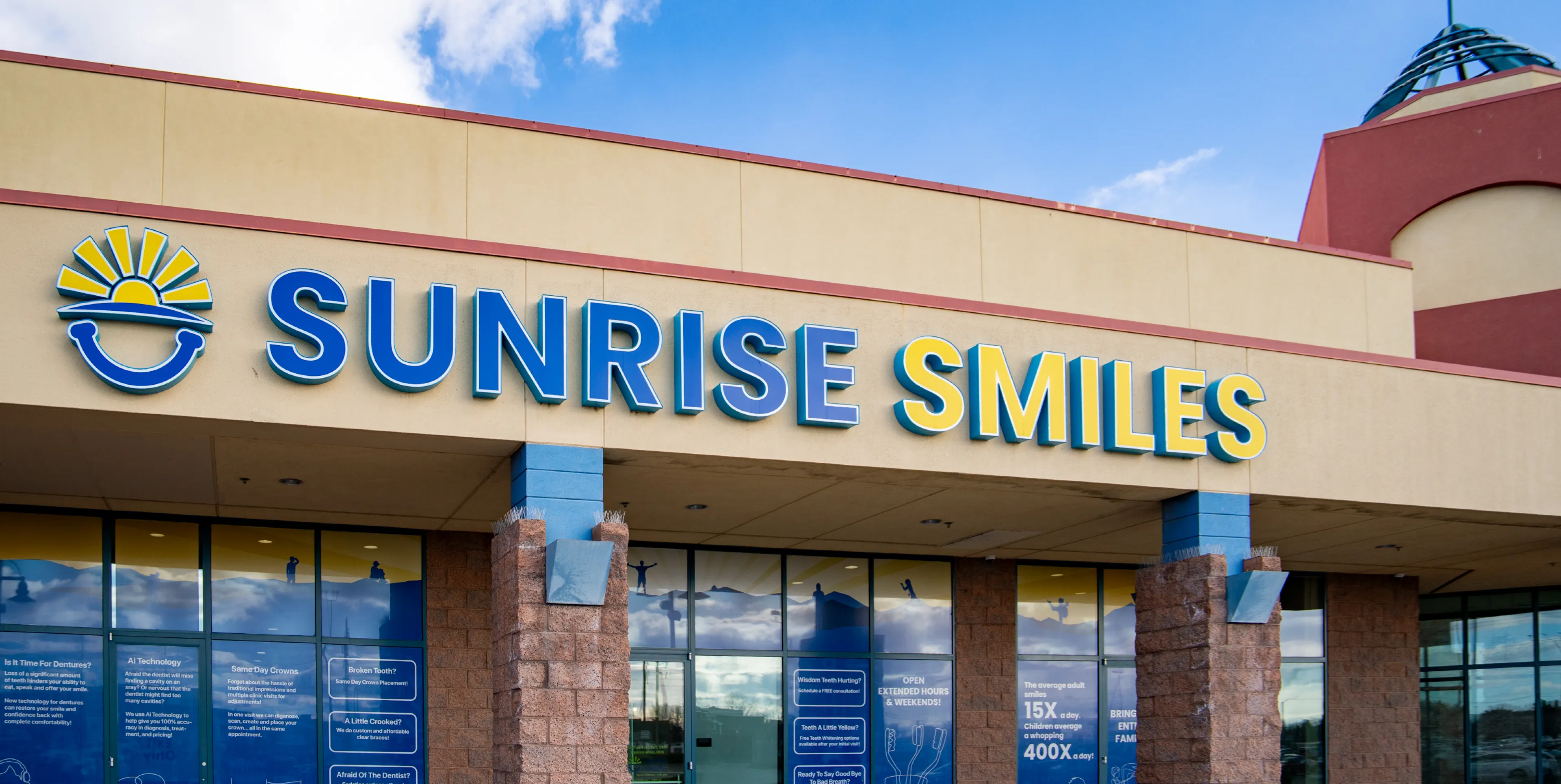 Exterior view of Sunrise Smiles dental office with blue and yellow signage against a beige building.