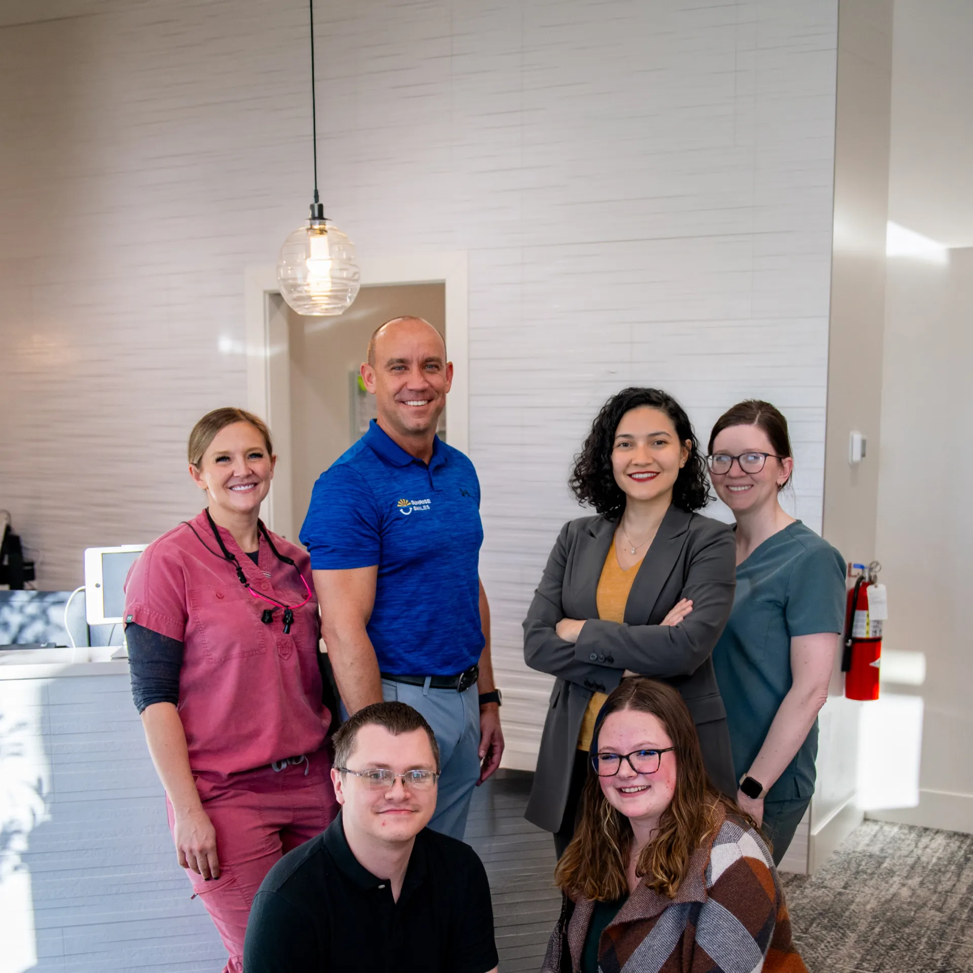 Group portrait of six smiling adults in a modern office setting.