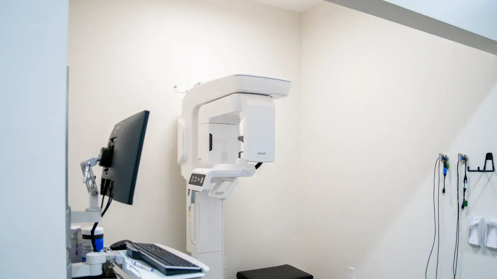 Dental imaging room with a Vatech panoramic X-ray machine, a computer monitor, keyboard, and hanging cords.