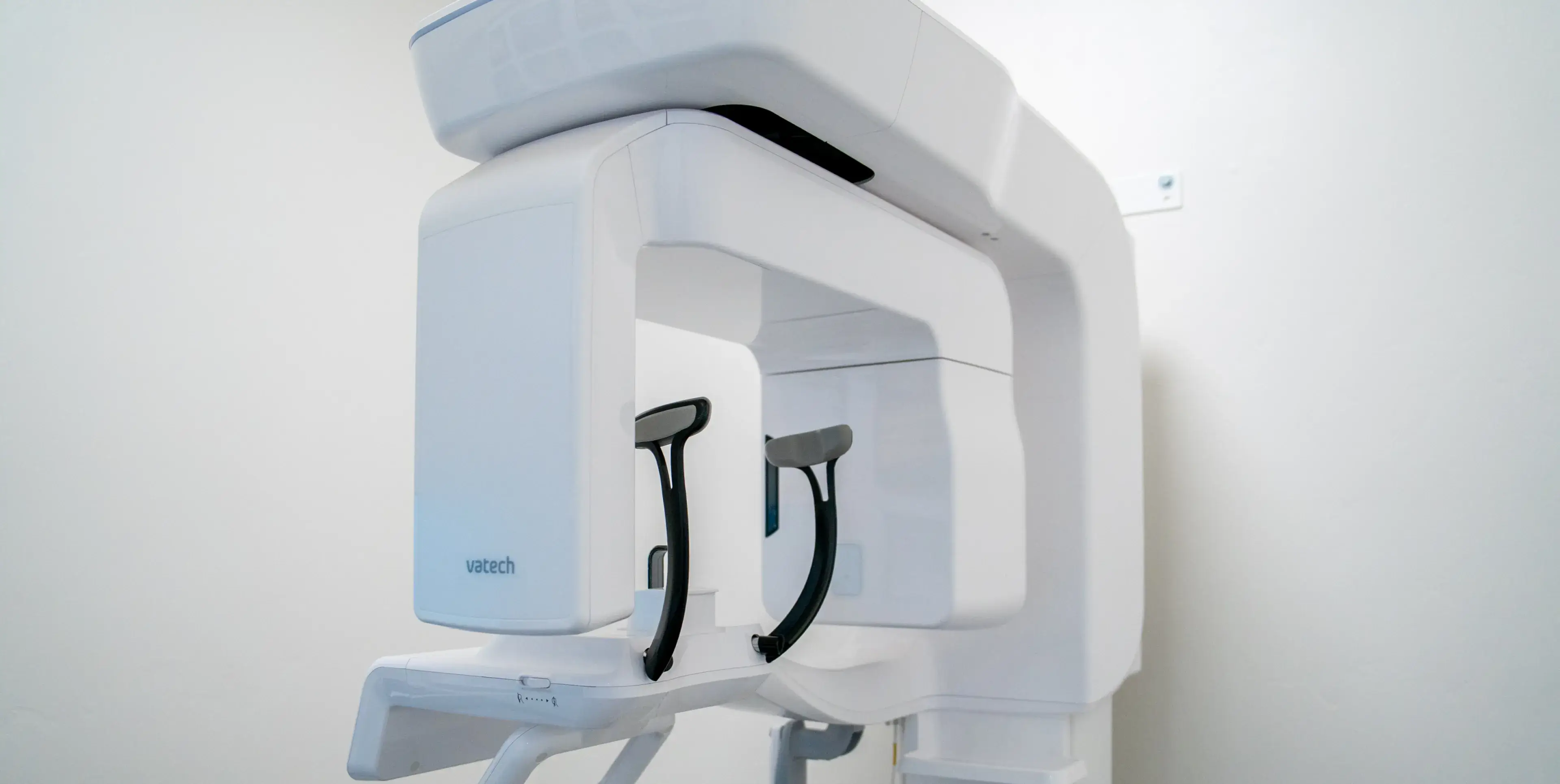 Modern white dental panoramic X-ray machine with black patient head supports in a clinical setting.