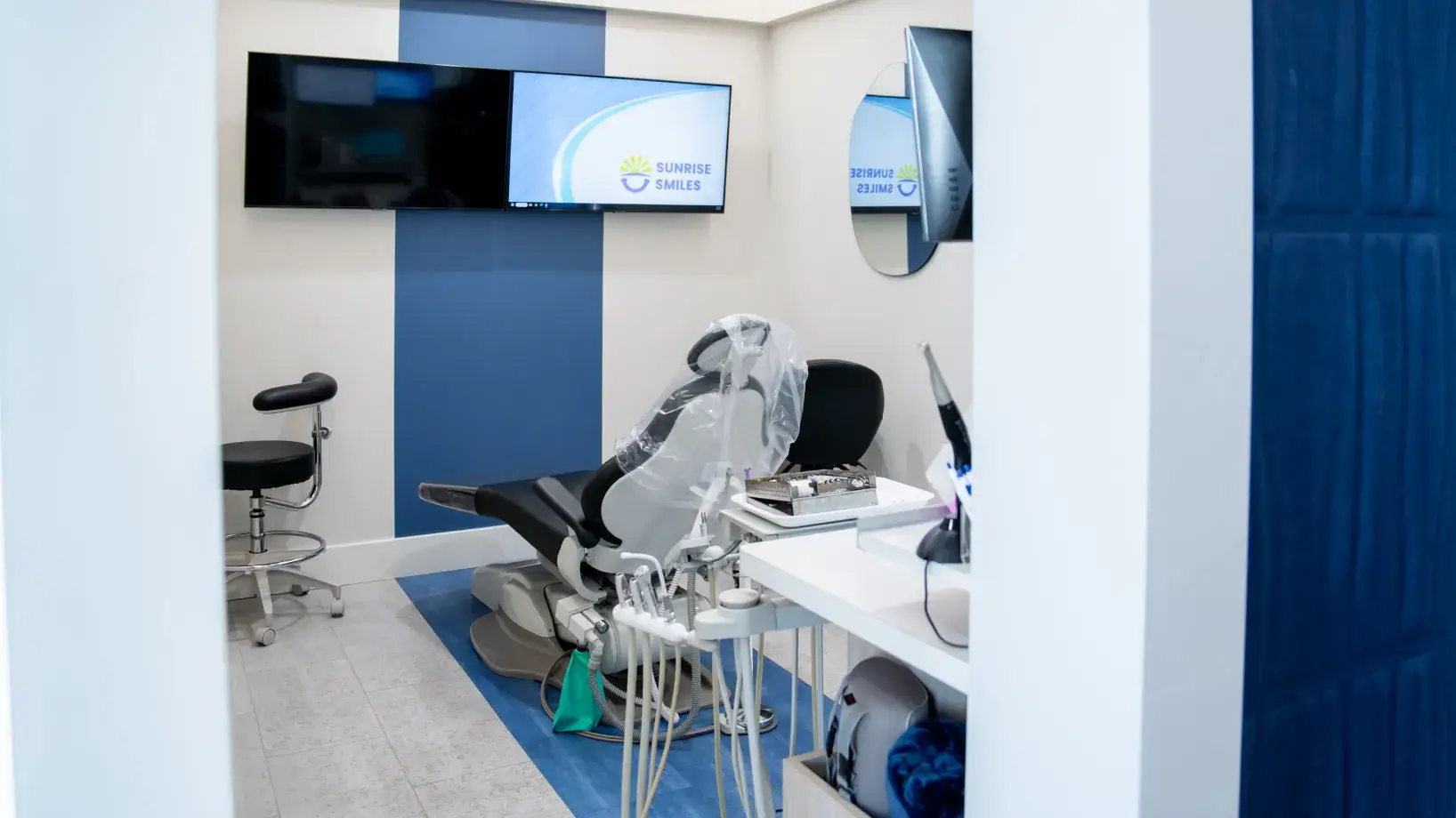 Modern dental treatment room with dental chair, equipment, and a screen displaying Sunrise Smiles logo.
