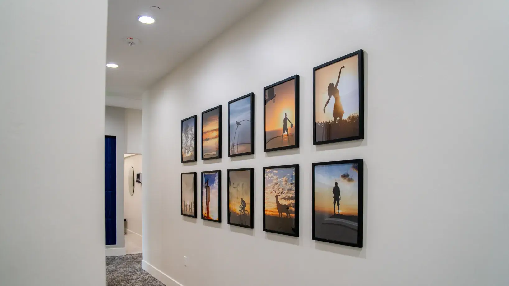 Hallway wall decorated with two rows of framed silhouette photographs featuring people and nature at sunset.