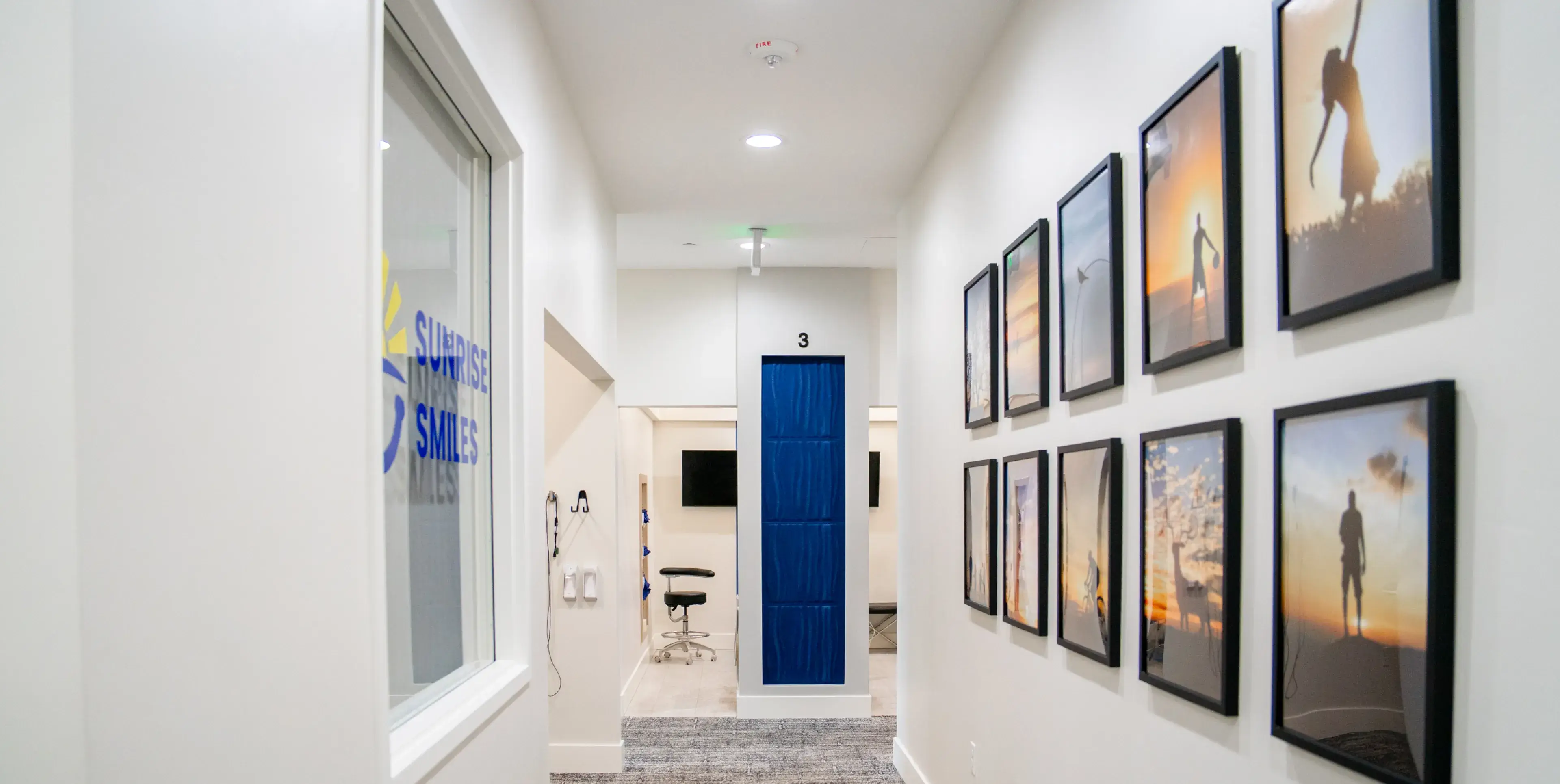Bright hallway with a window on the left showing 'Sunrise Smiles' logo and a corridor with framed sunset silhouette photos on the right wall.
