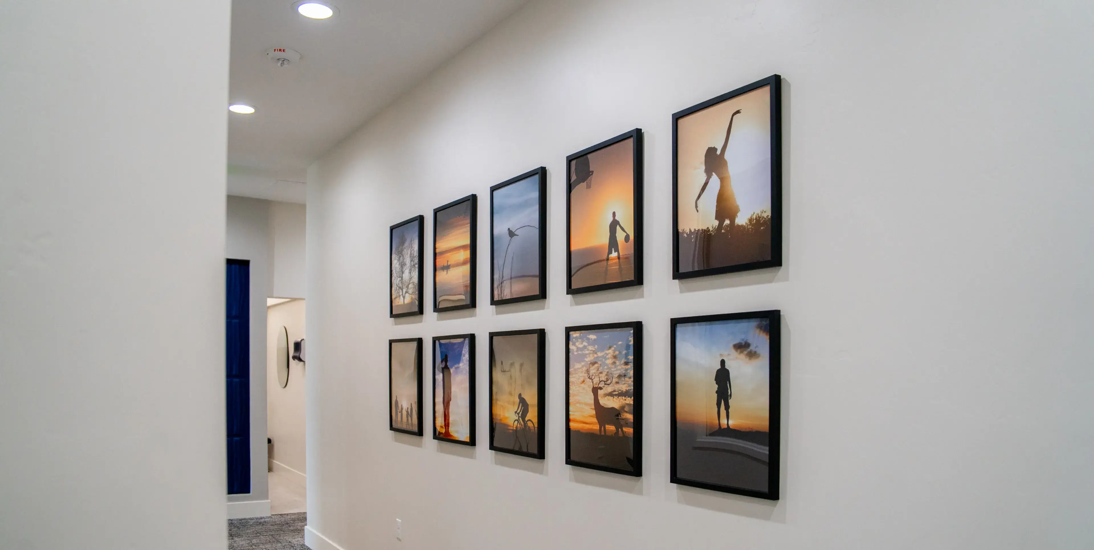 White hallway wall decorated with ten framed pictures showing various silhouette scenes at sunset or sunrise.