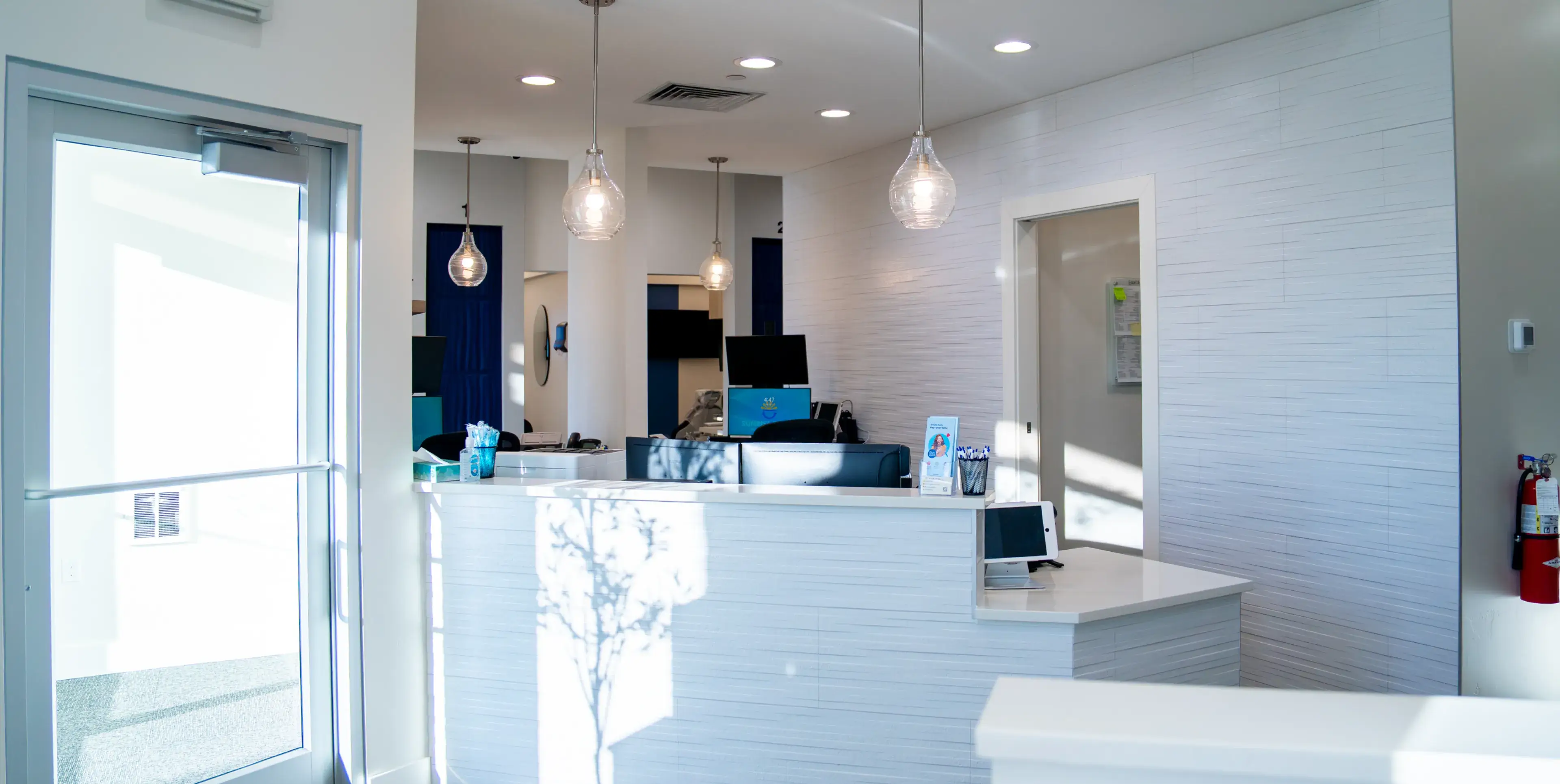 Bright modern reception desk with computers, pendant lights, and a glass door entrance in an office.