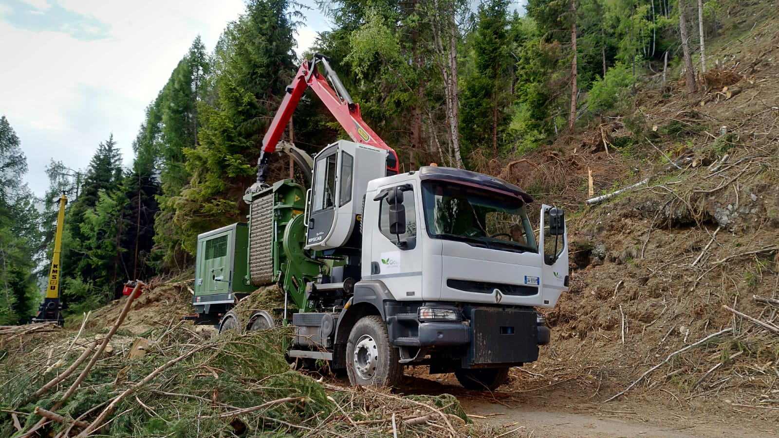 White forestry chipper truck with red crane arm in a forest clearing with tree debris around.